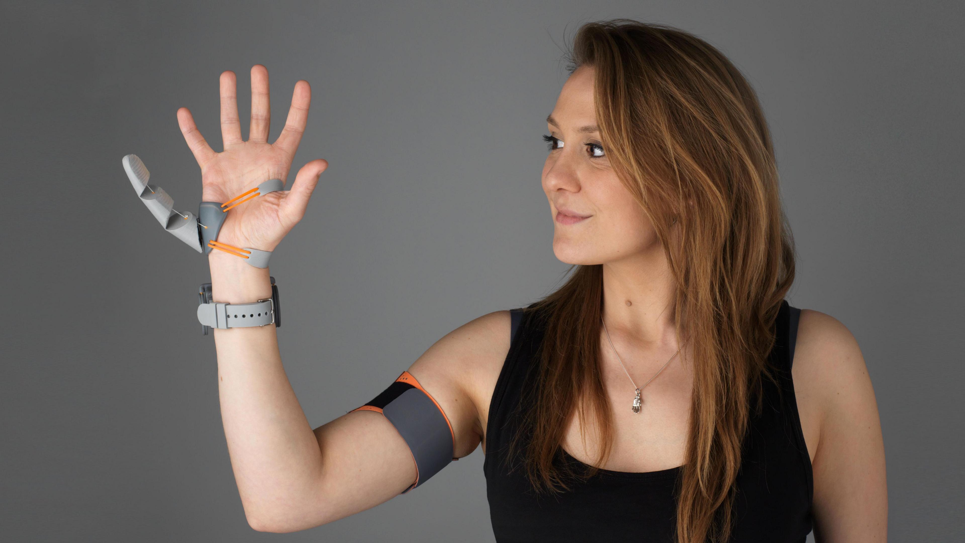 Dani Clode wearing the Third Thumb she designed. It is made of plastic and is attached just below her little finger, with a band around her upper arm connected to it