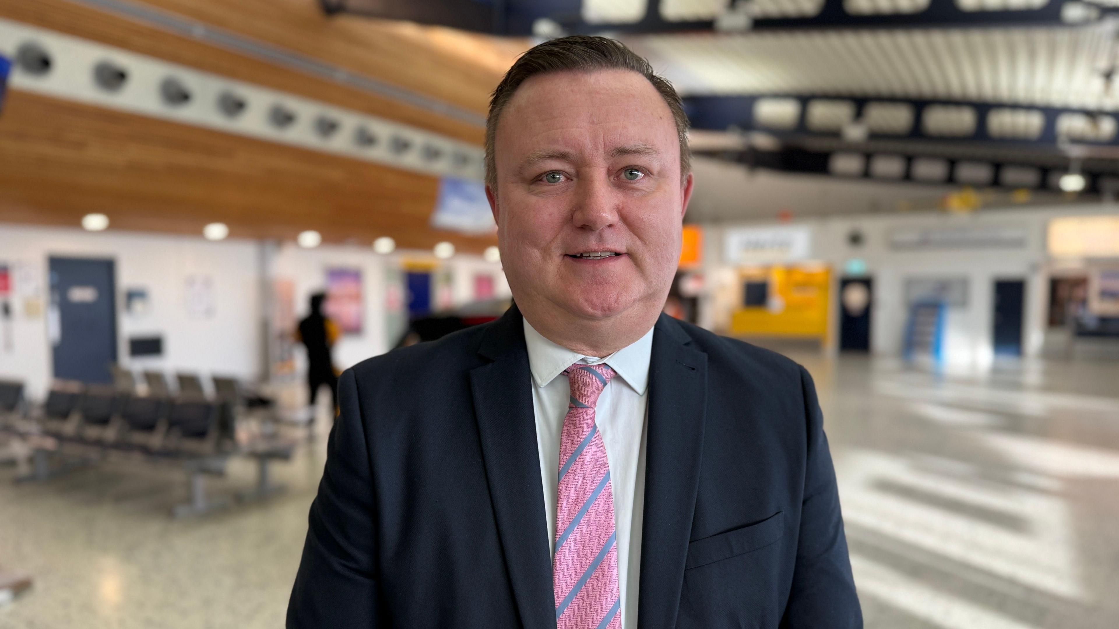 Richard Thomasson - a man wearing a suit and tie standing inside Guernsey Airport.