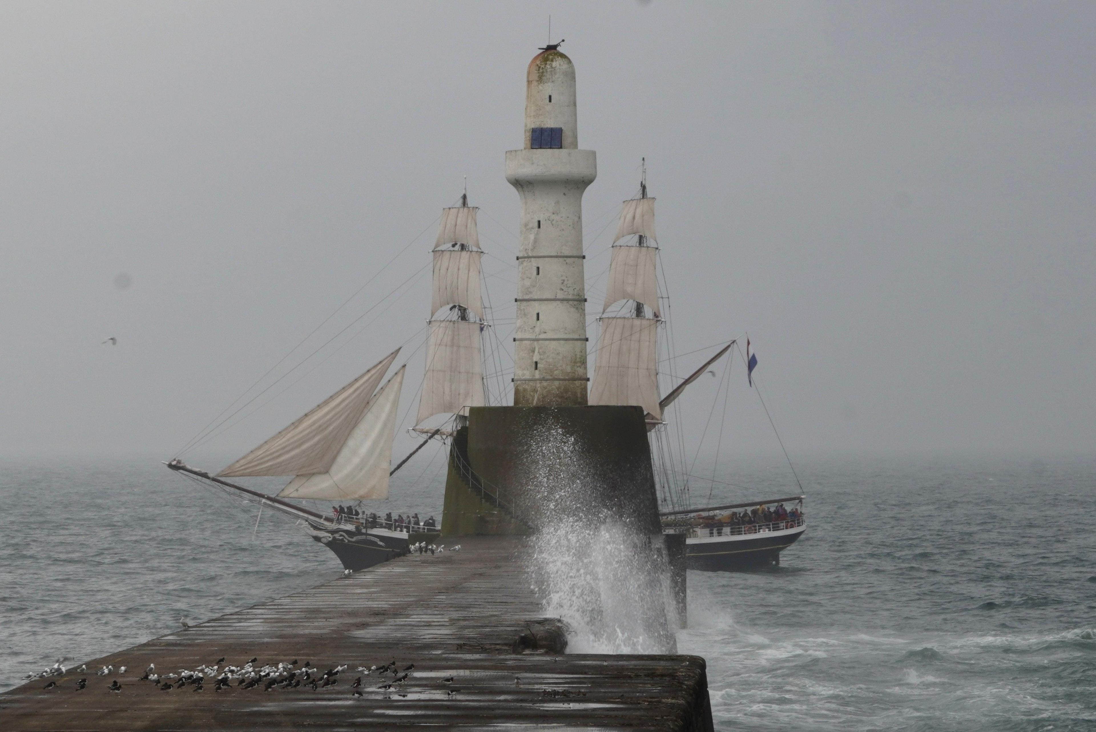 A ship sailing past a lighthouse on a stormy day with grey skies