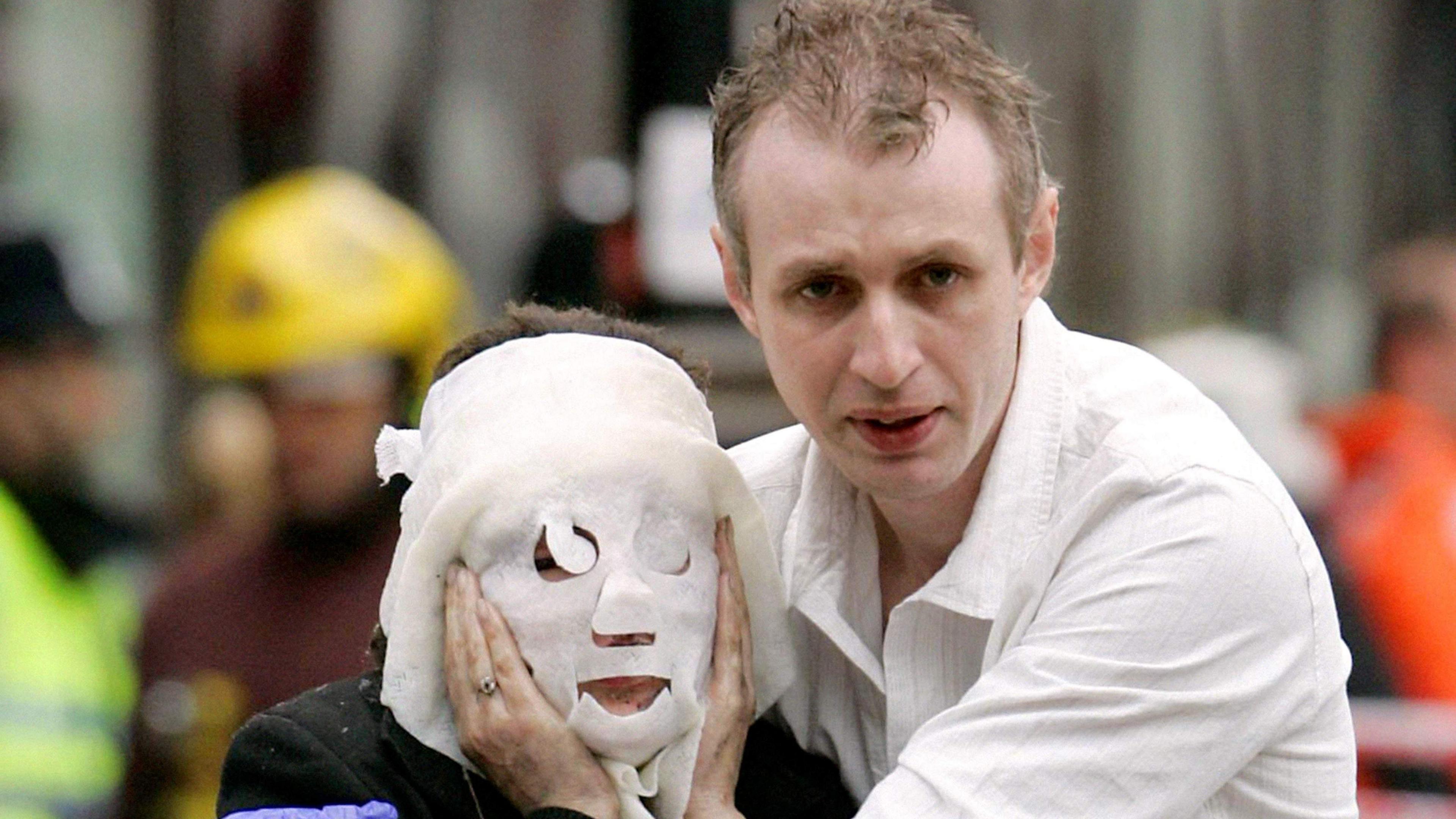 A woman wearing a burns mask to cover her face, walking through central London alongside a man with a worried expression, wearing a white shirt.