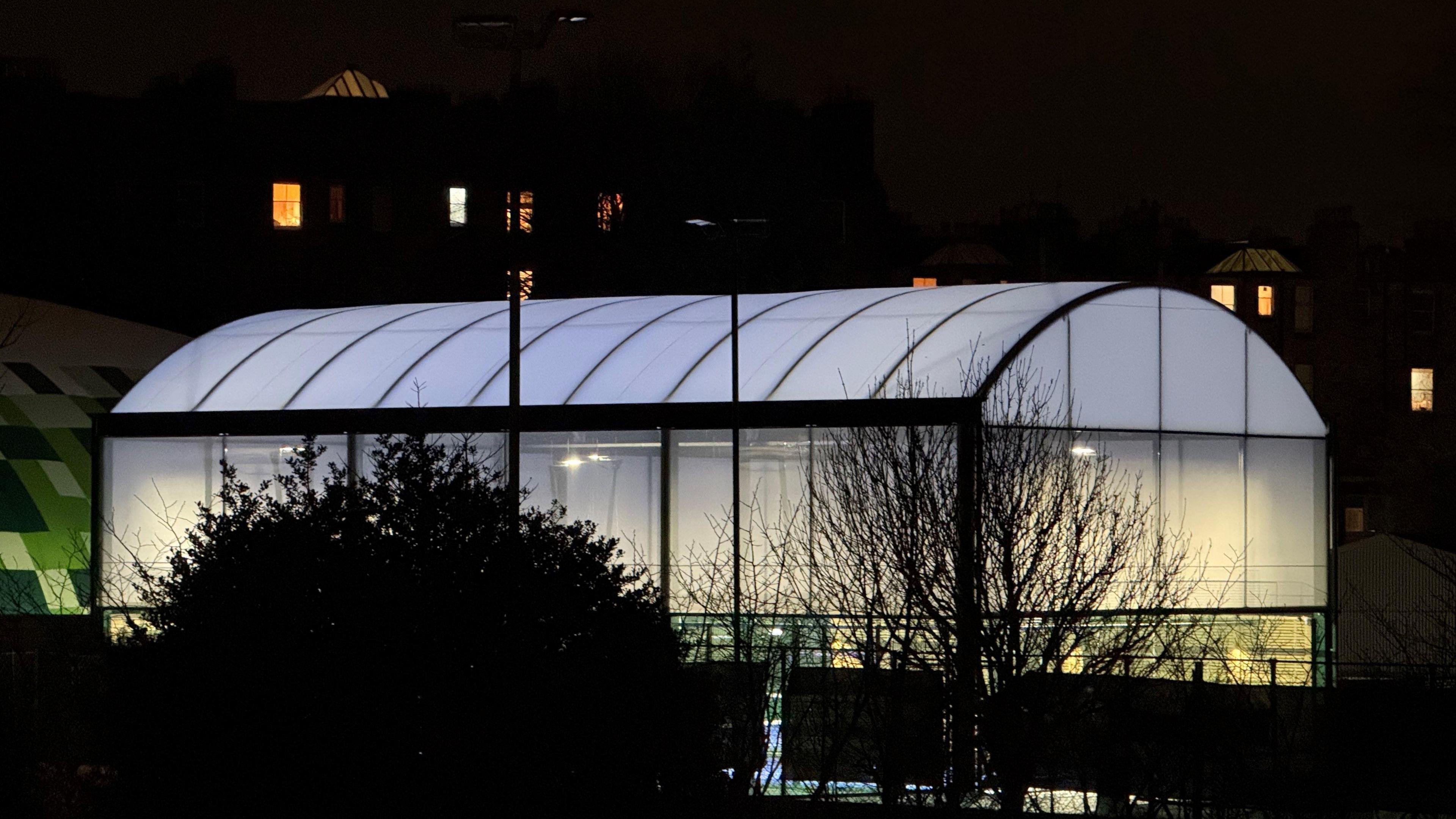 I very brightly lit indoor tennis court building glowing in the dark.