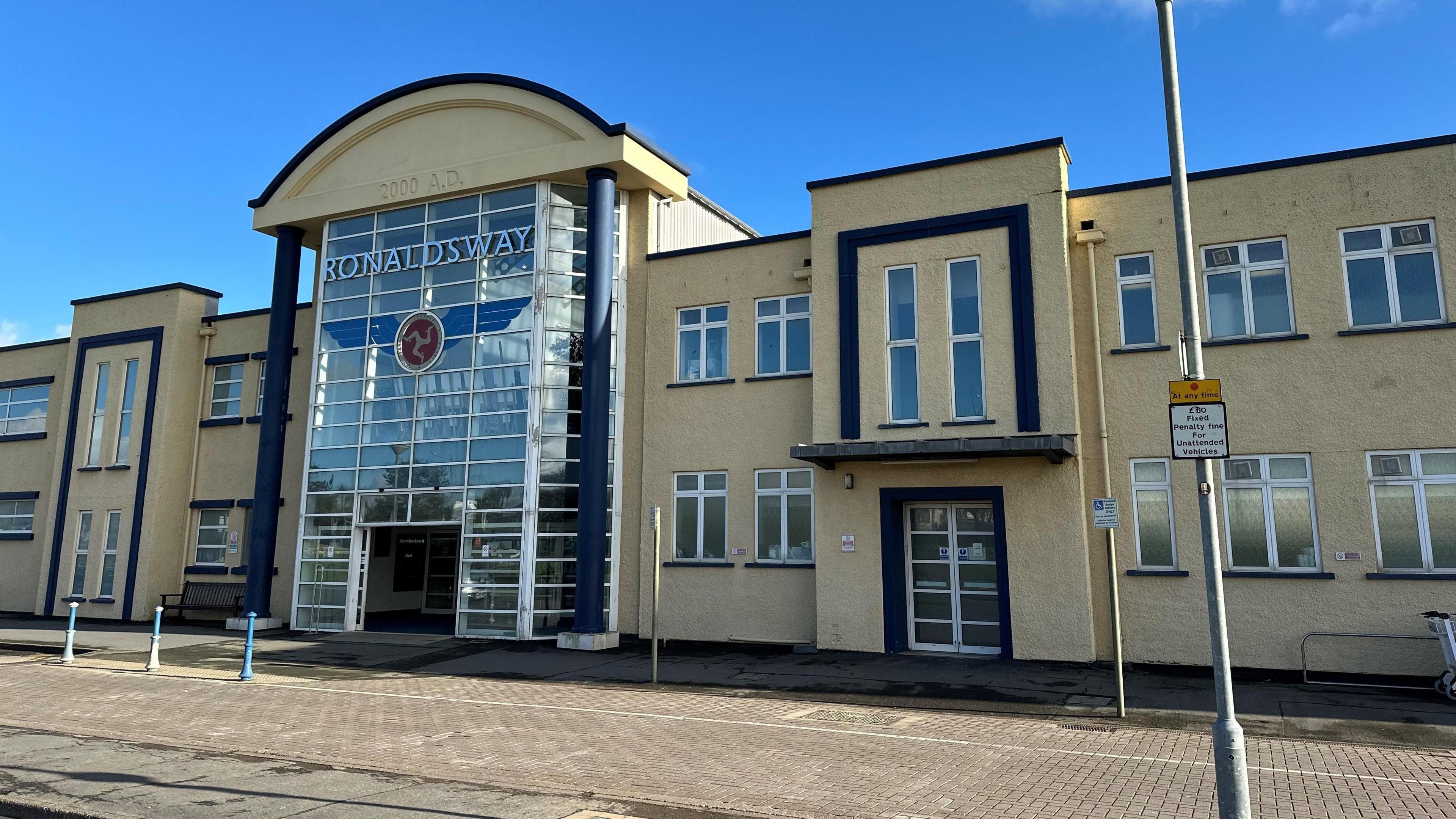 Pavement outside a beige building with a partial glass fronting with a sign that reads Ronaldsway