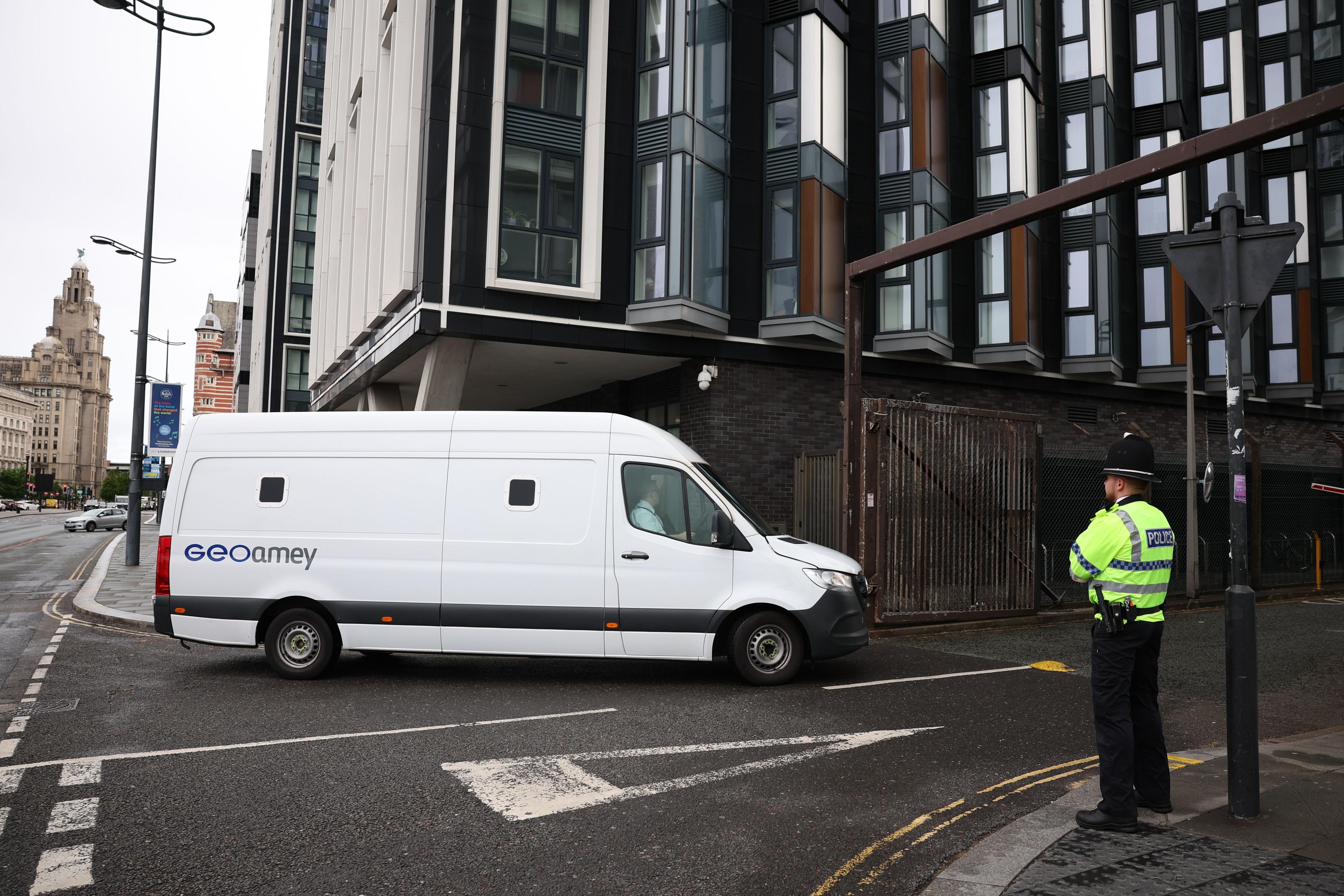 A white van turns into a road as a policeman stands watch