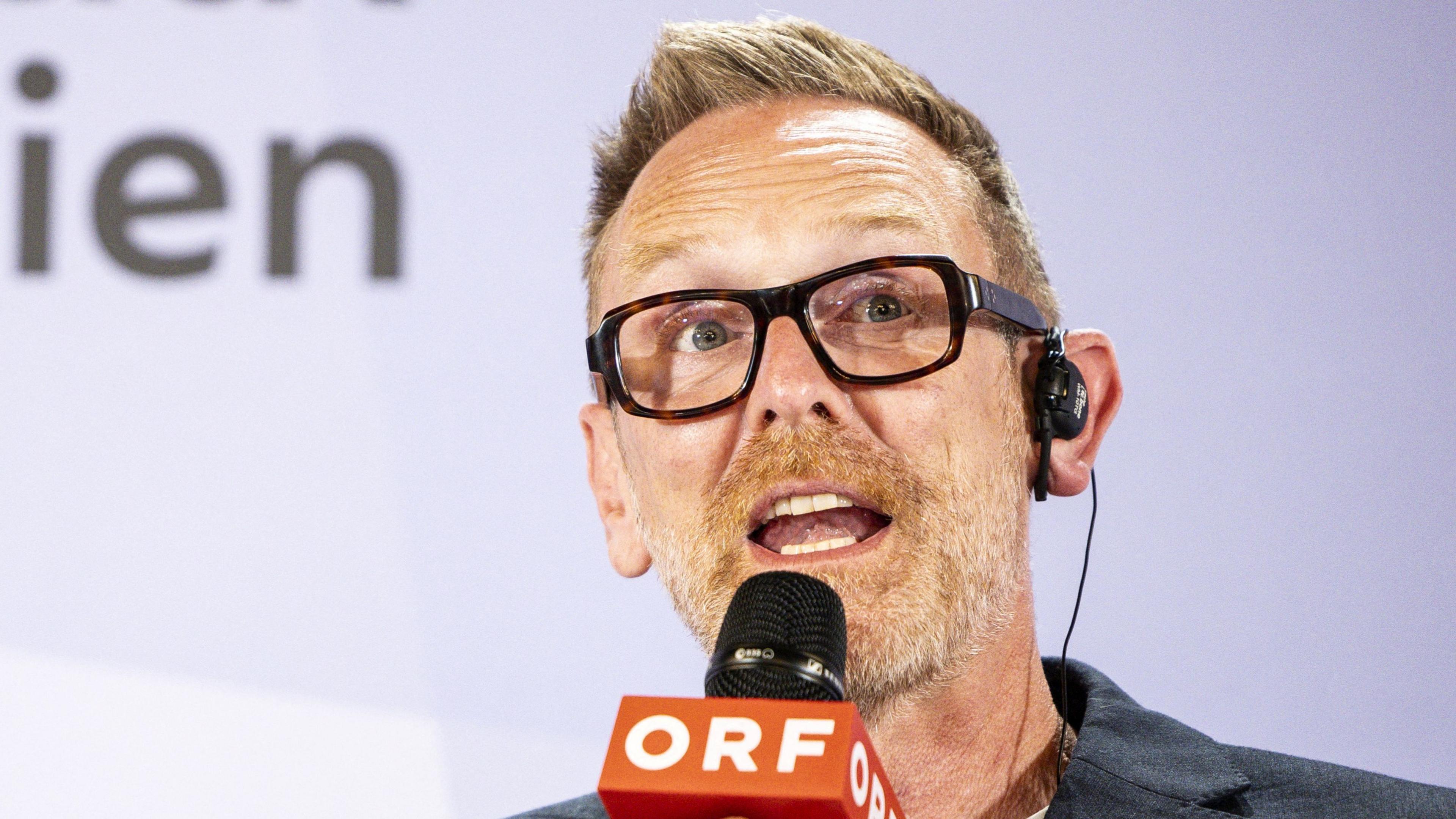 Martin Green, with spiky blond hair and dark thick-rimmed glasses, speaks into a microphone labelled ORF 