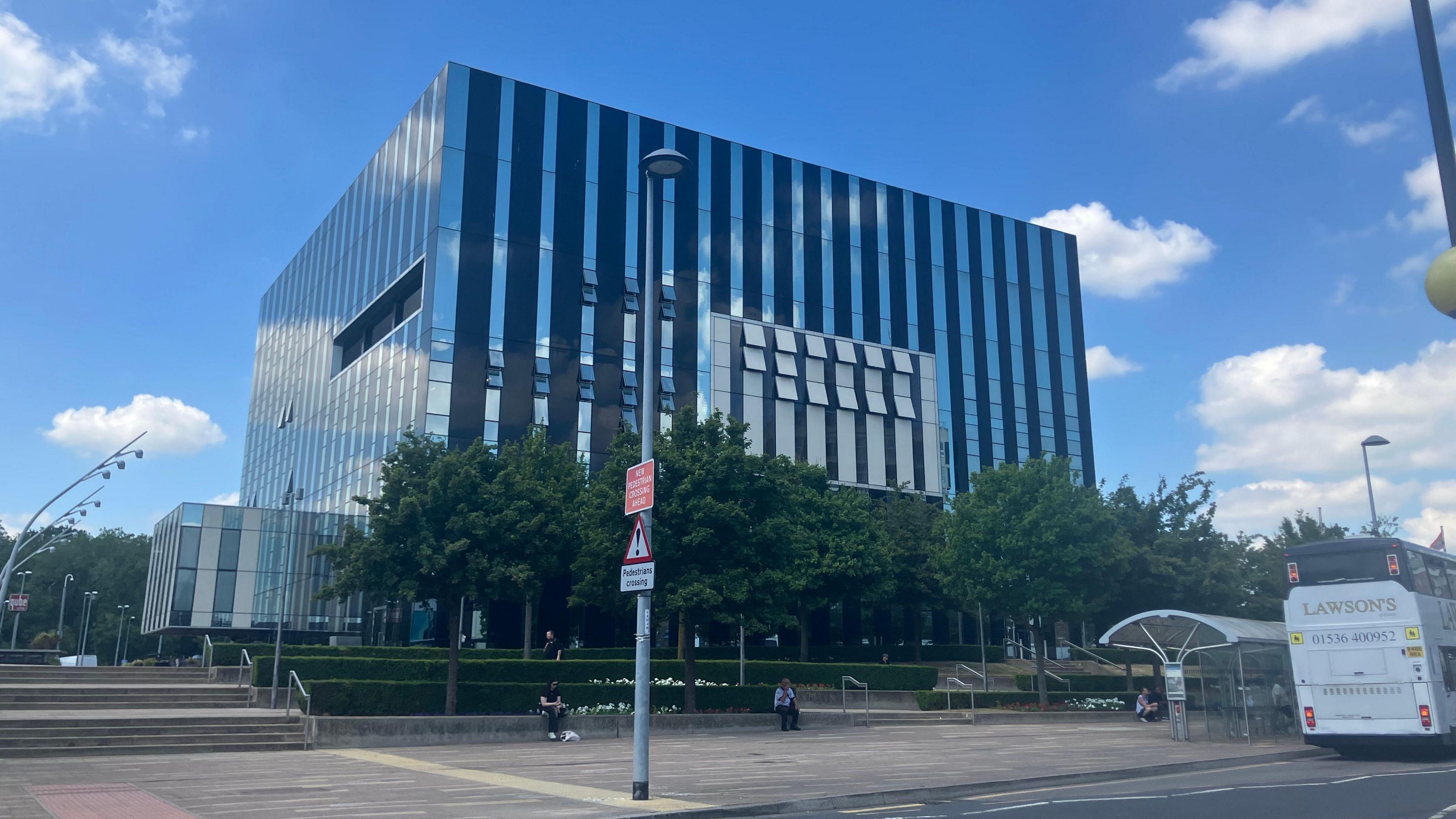 A glass building in a cube design in the middle of a town square.