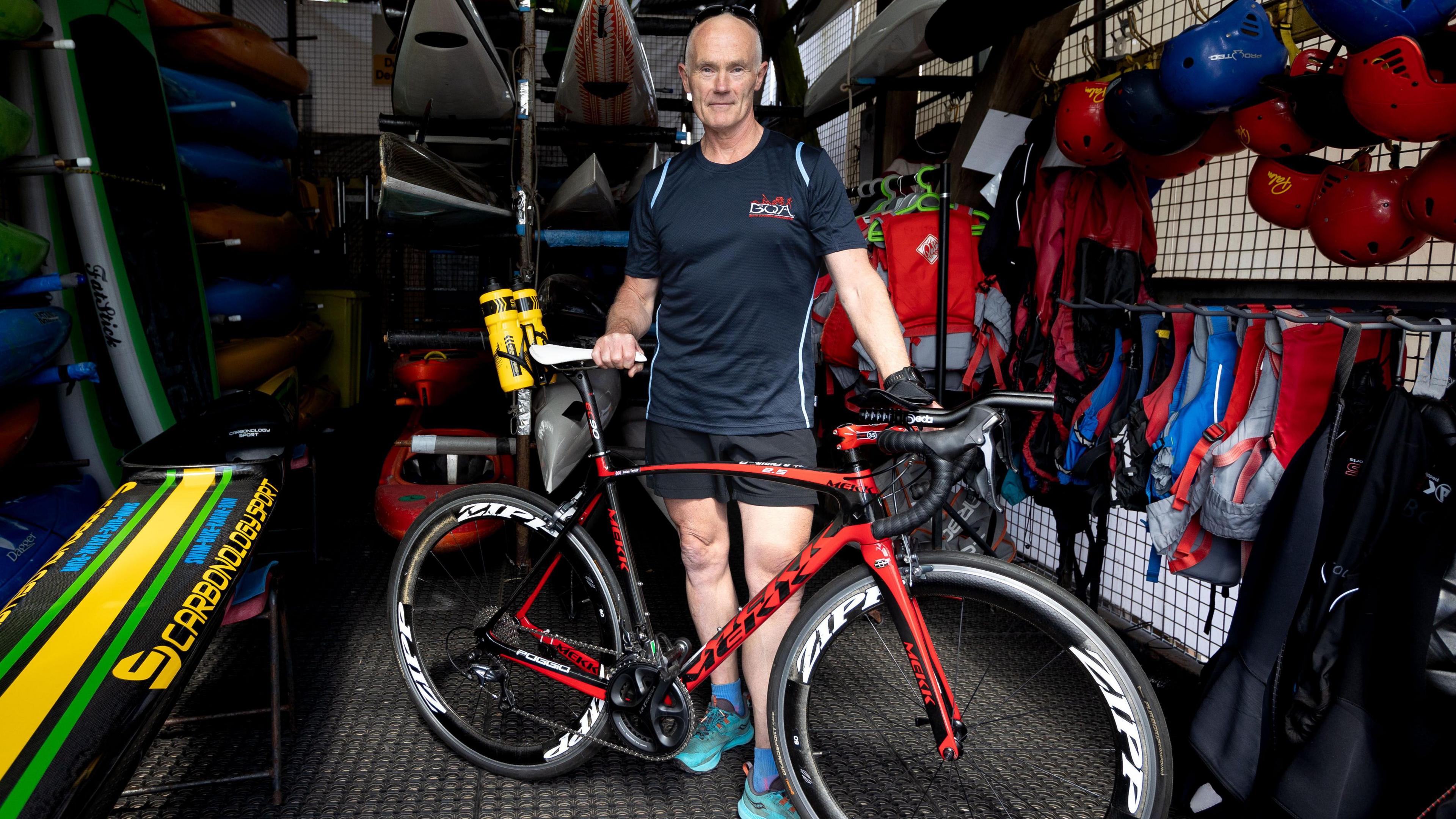 Jules Taylor standing in a room full of kayaks, posing in front of a bicycle