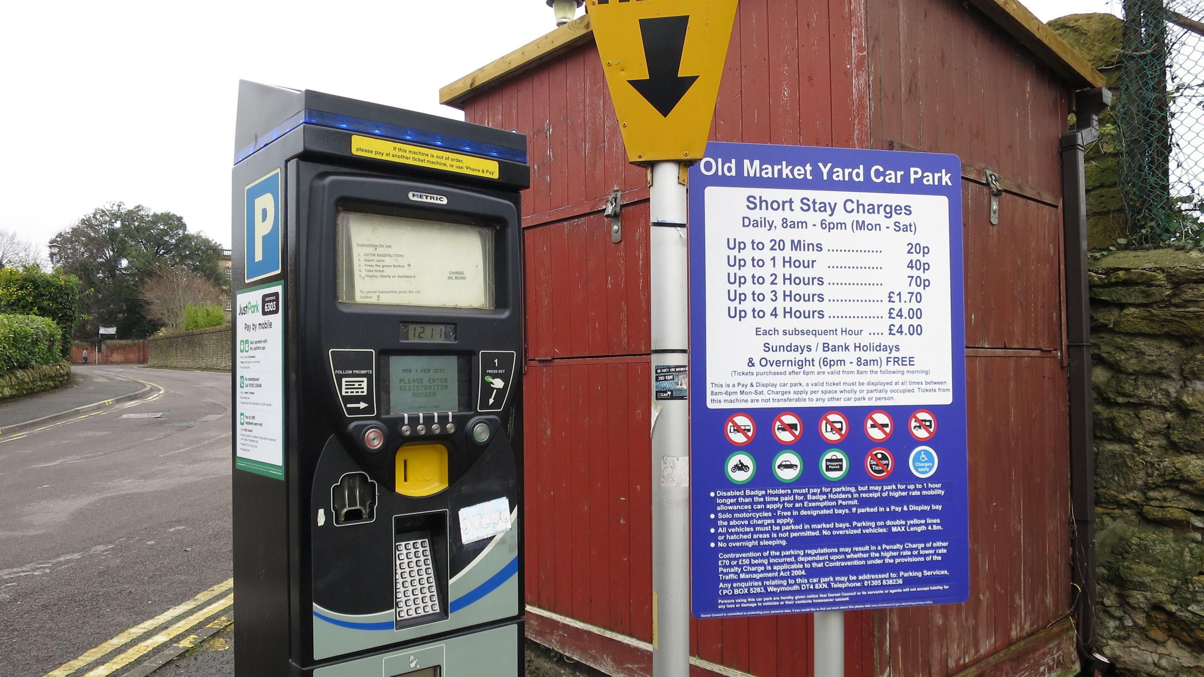 A black parking meter next to a sign explaining the parking charges at Old Market Yard car park in Sherborne