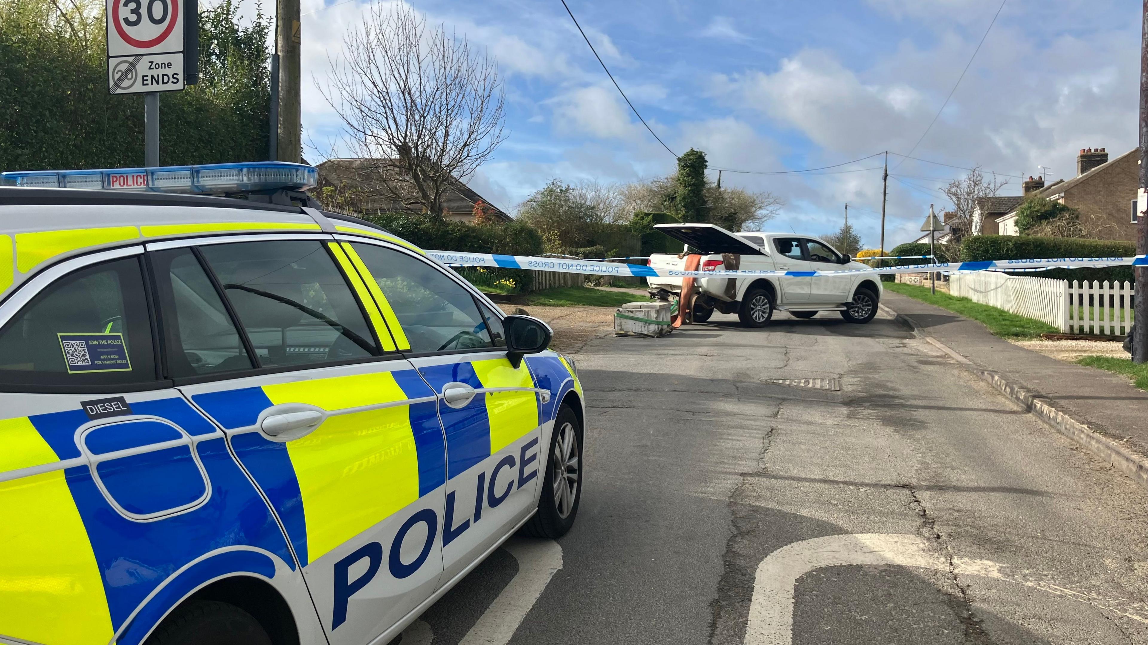 A police car parked in the foreground, and the pick-up van left in the background in the middle of a residential road