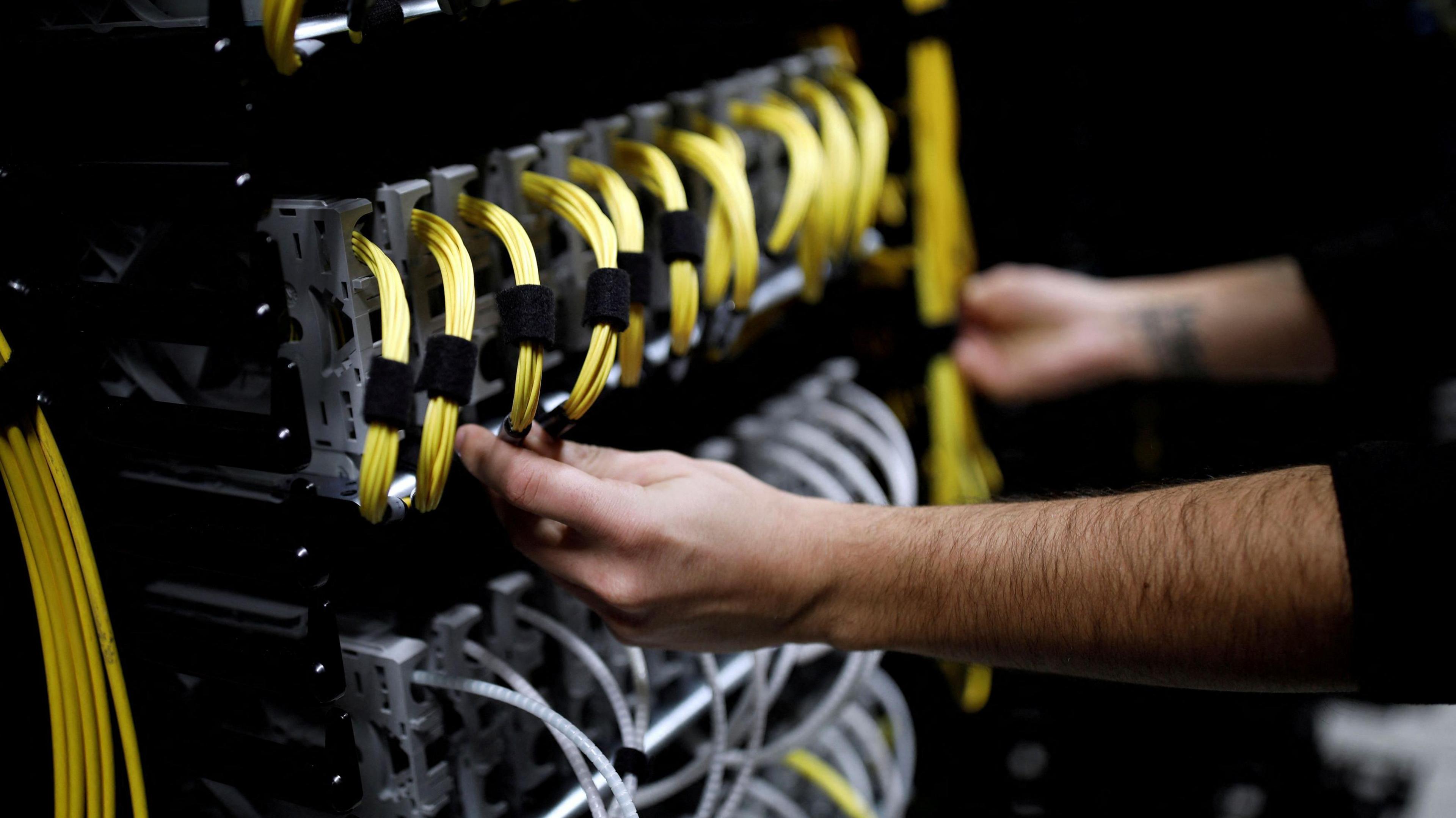 A man's hands adjust wires on an internet server