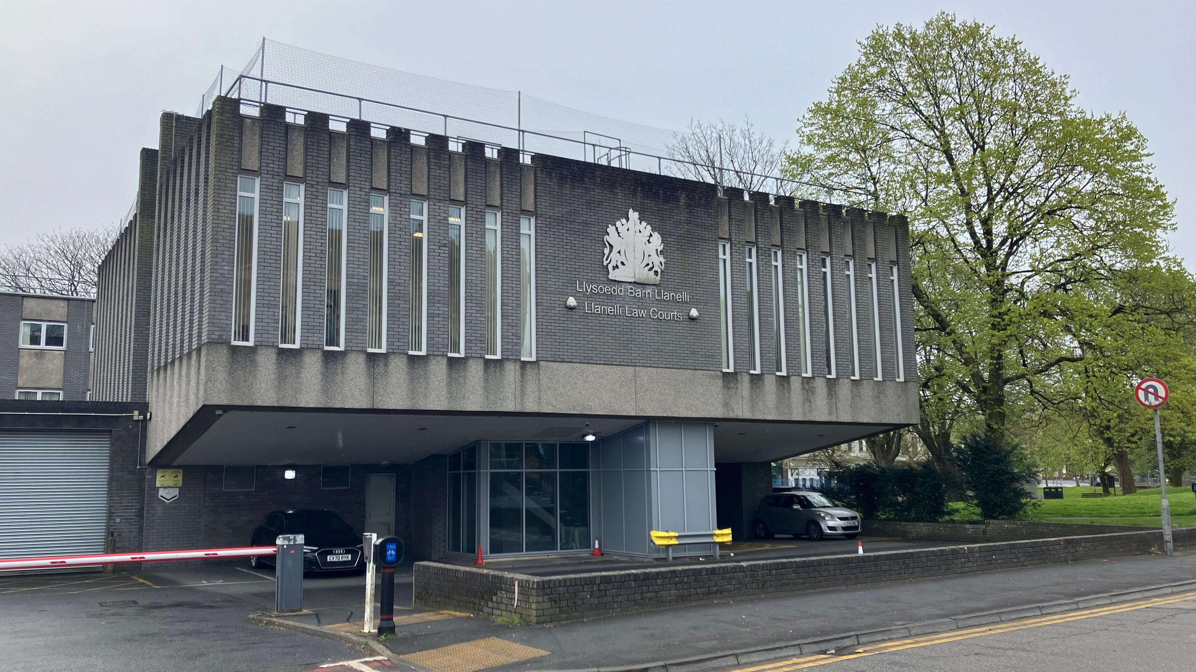 A photo of the exterior of a court of law building with a tree and a road sign on the right-hand side