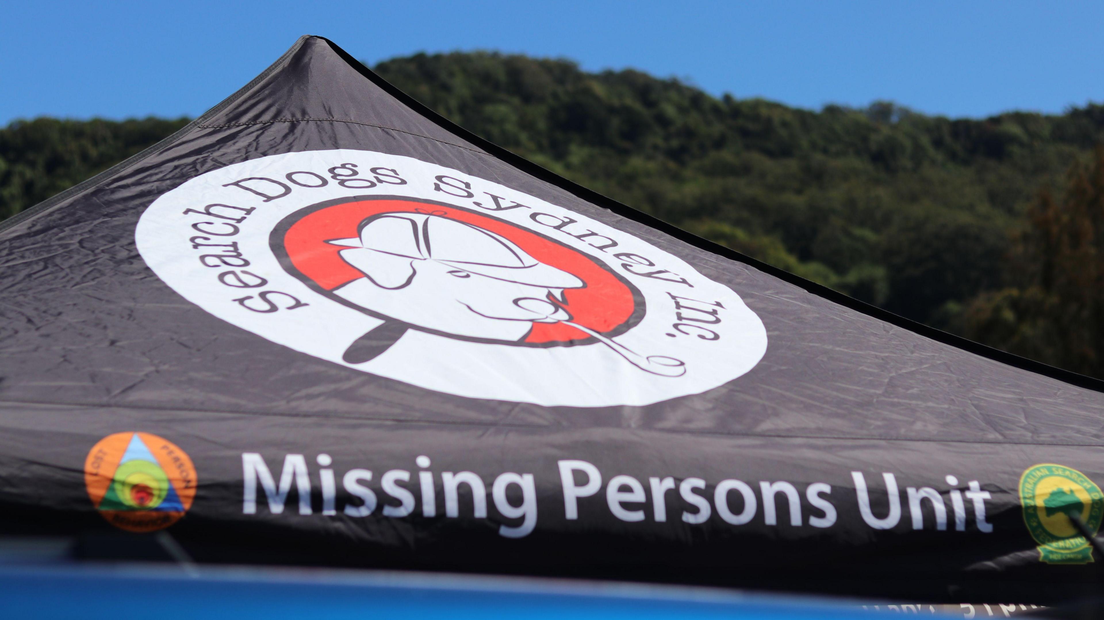 The top of a black tent reads "Missing Persons Unit"
