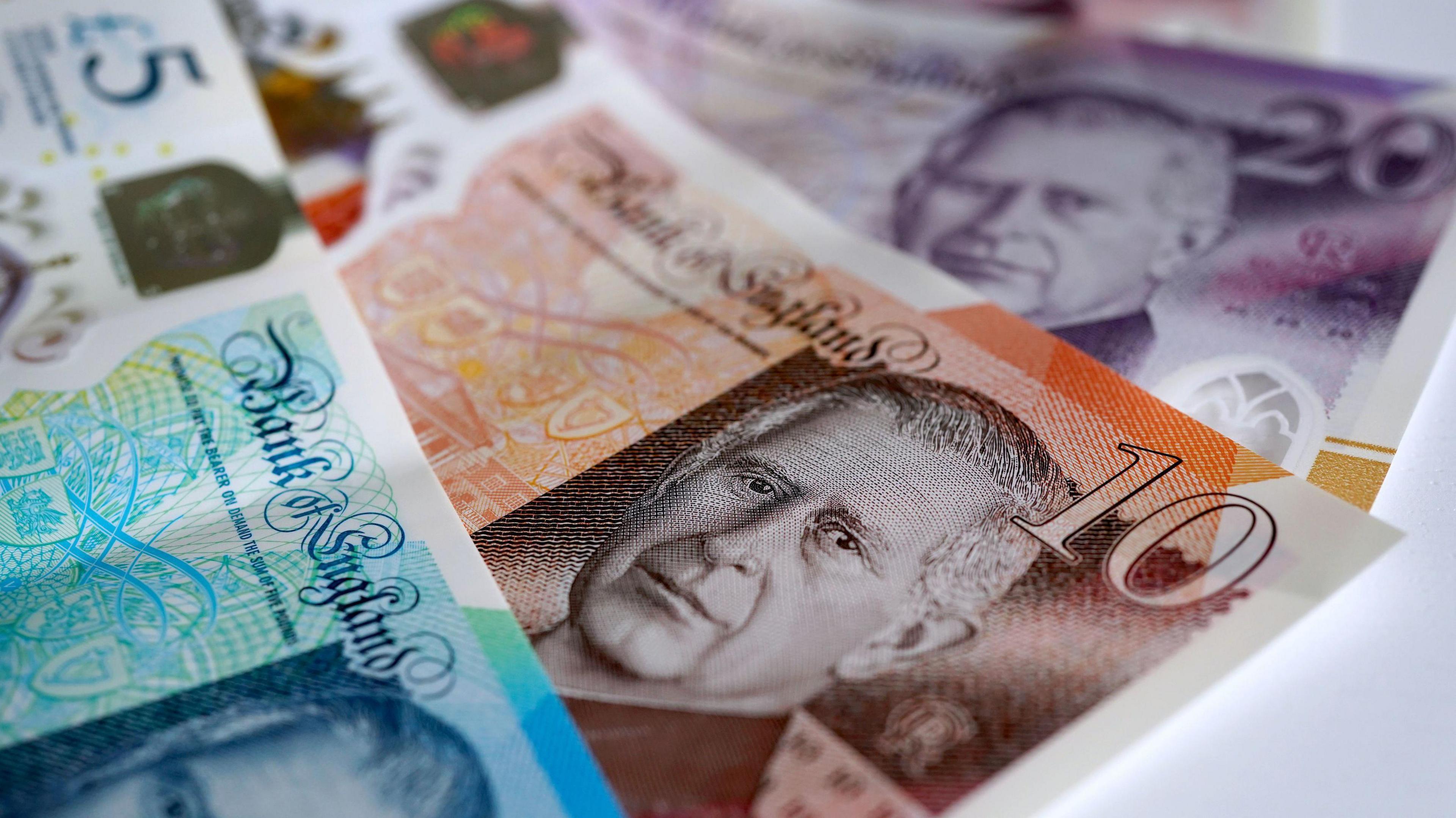 Three banknotes lying on a table - a £5, £10 and £20 overlap each other