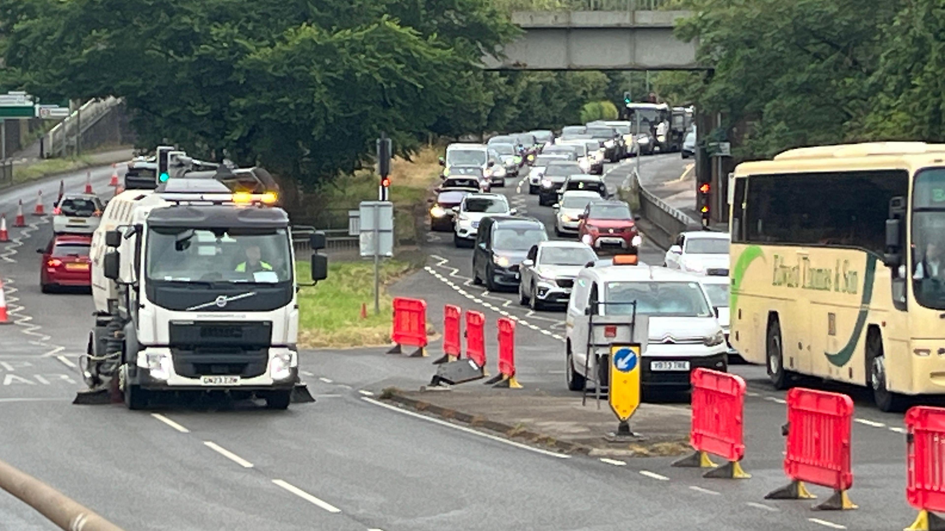 A street cleaner on one side of the road and queuing traffic