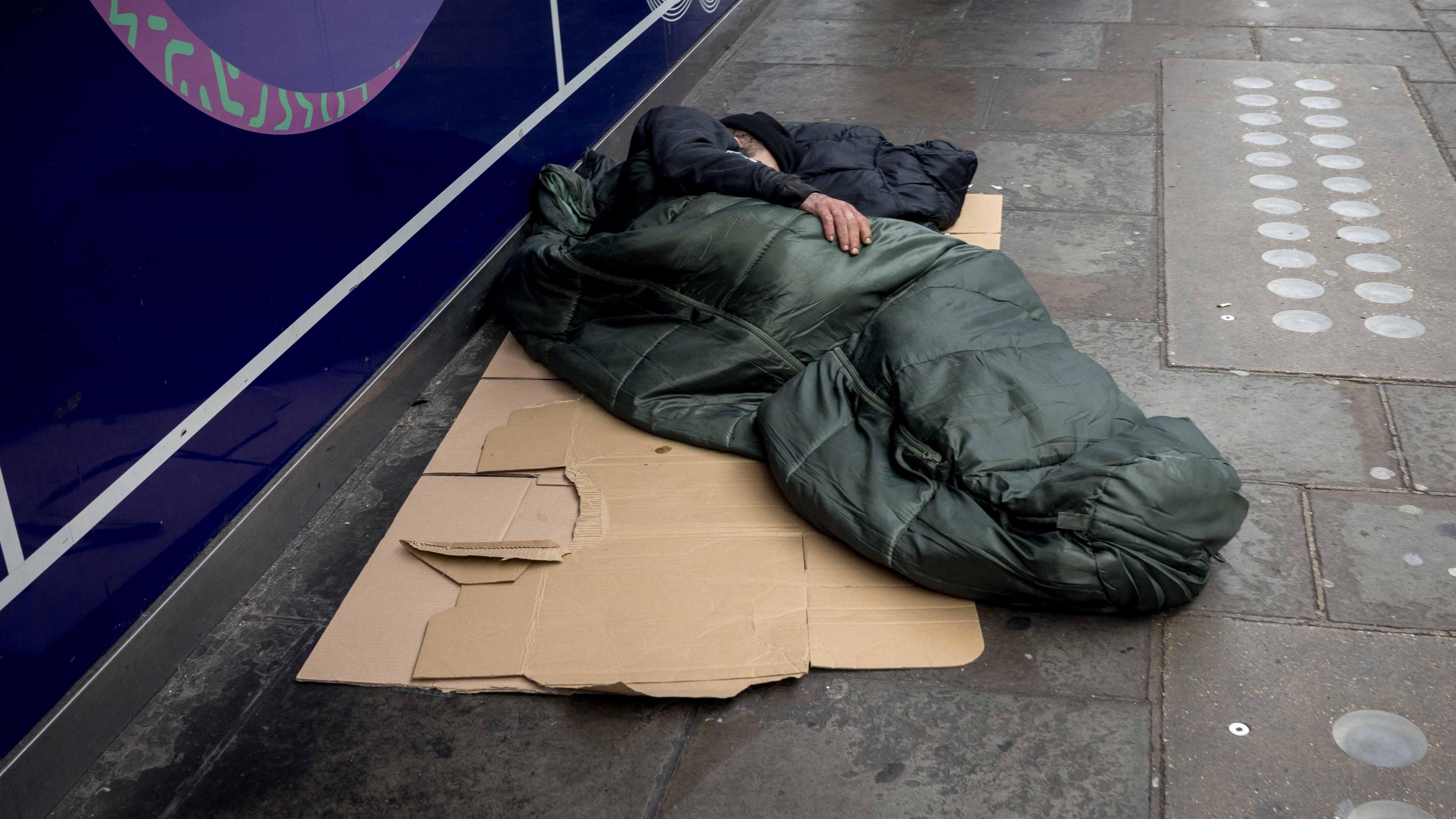 Generic picture of a homeless person sleeping on the streets in a sleeping bag on a piece of cardboard.