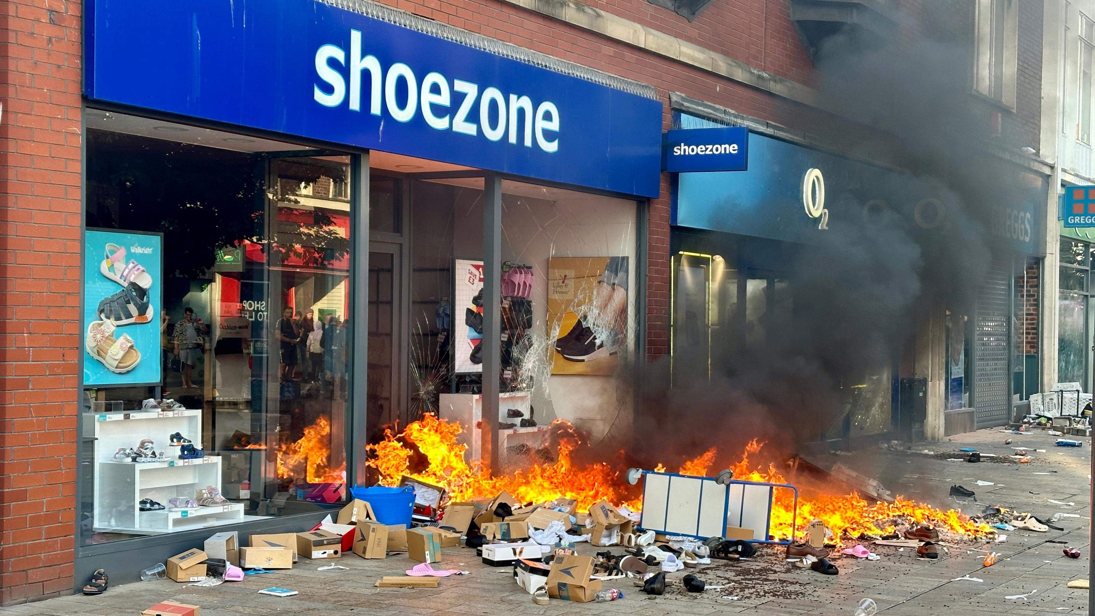 Shoes and shoeboxes are on fire outside the Shoezone shop, which has broken doors and windows.