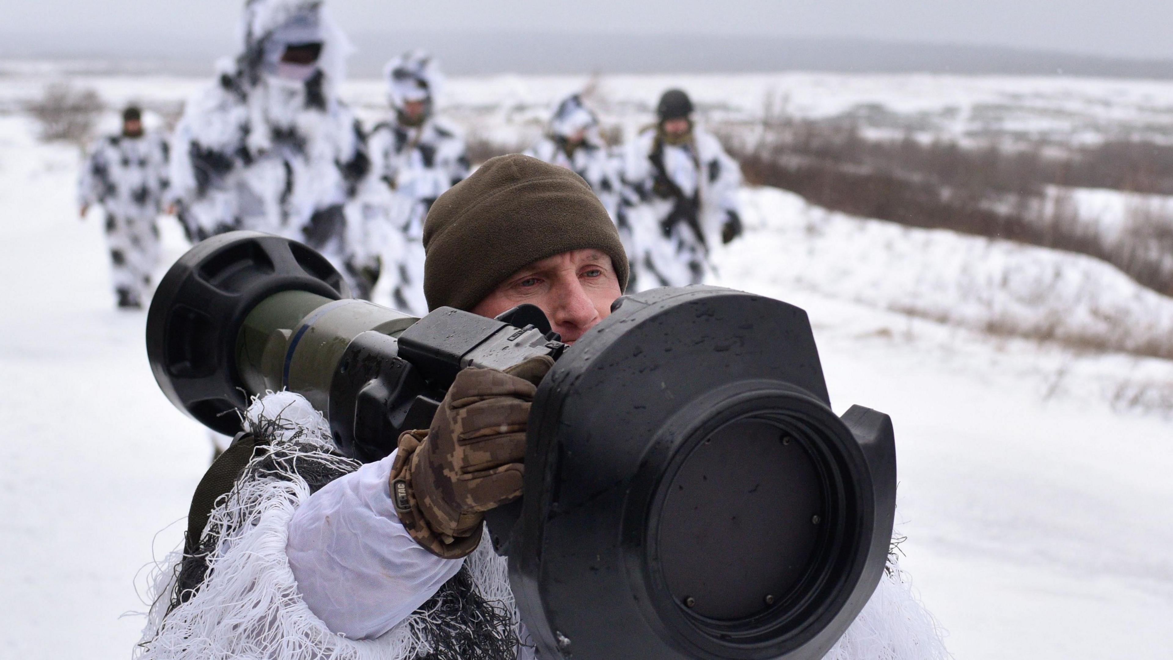 A Ukrainian soldier armed with a British NLAW anti-tank missile. The background is snowy and his colleagues are wearing winter camoflage.