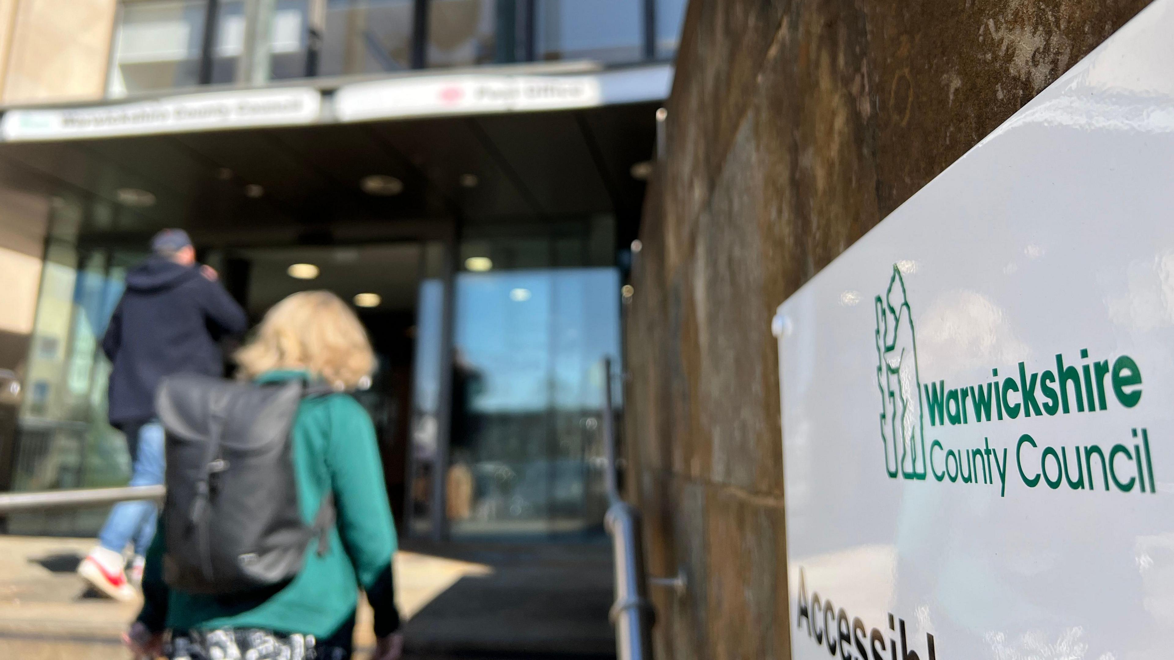 Image of people walking into the entrance of Shire Hall, Warwick. A lady in a green coat ascends stairs.