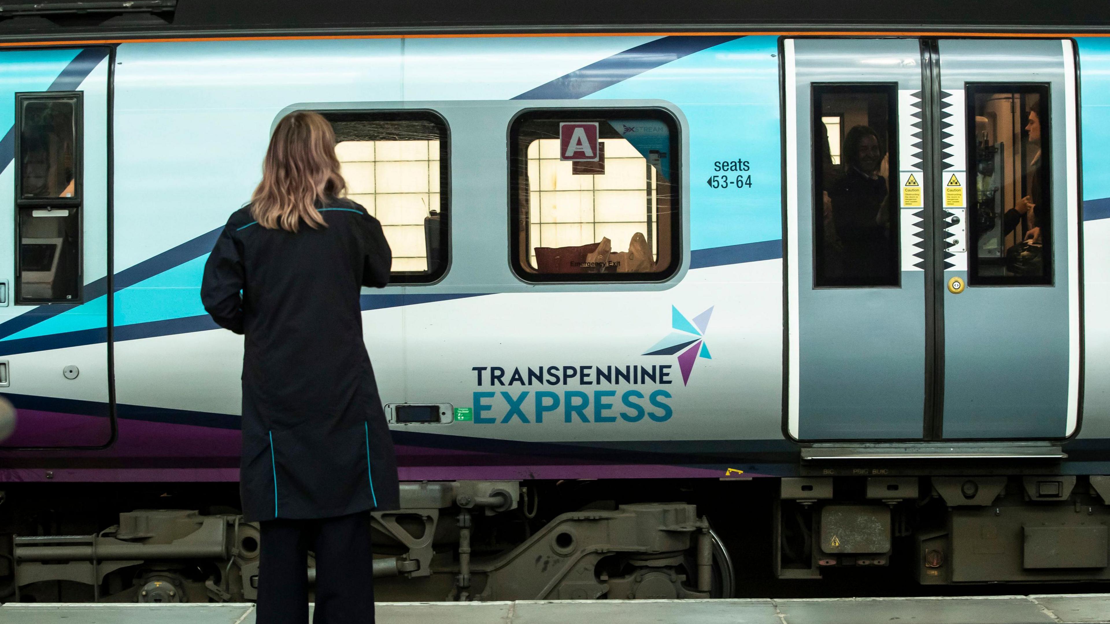 A woman standing on a platform in front of a TPE train