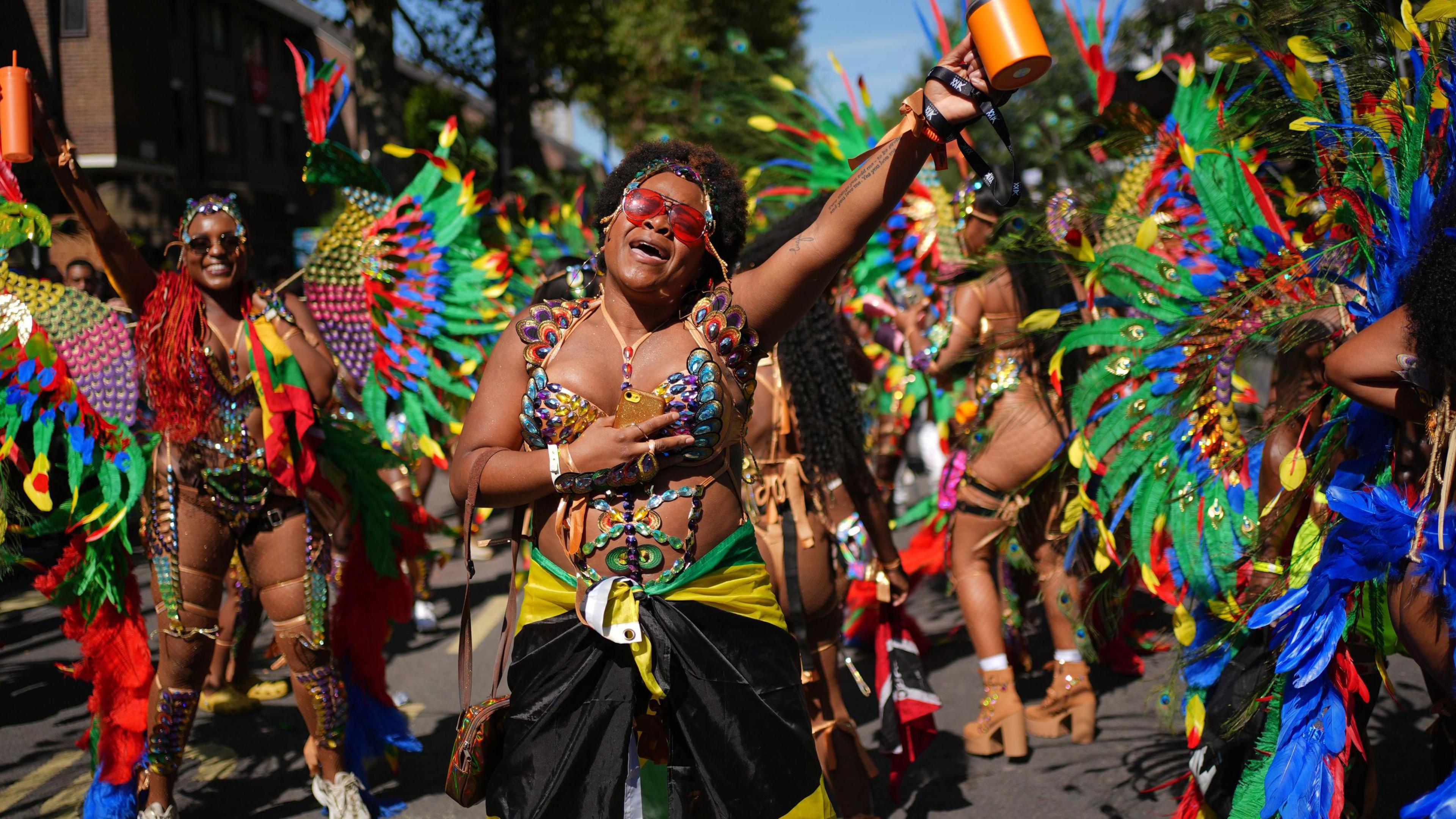 A group of women in bright costumes perform in the street. One woman at the front appears to be singing.