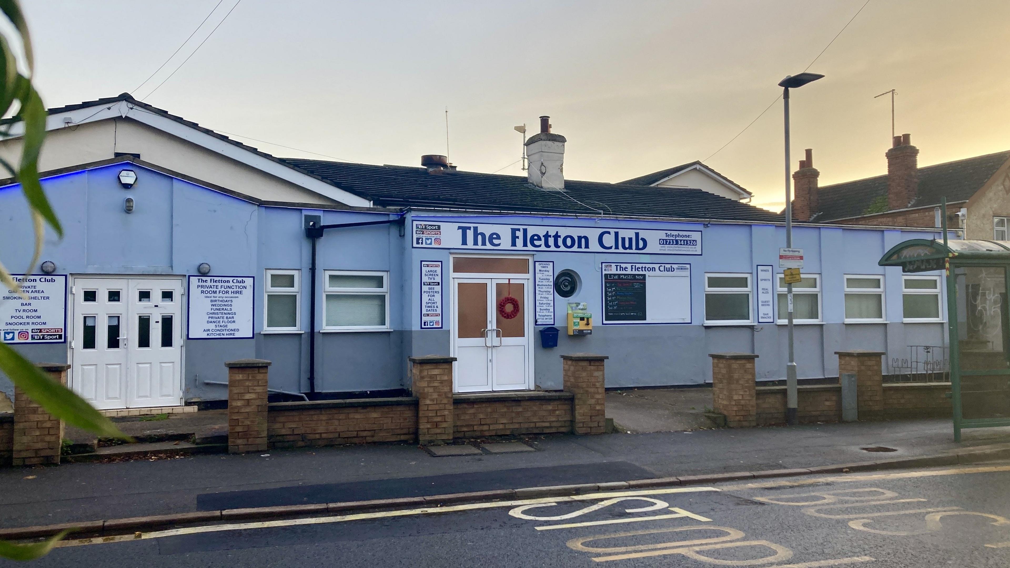 The Fletton Club is a one-storey building painted light blue with a bus stop in the foreground covered in graffiti.