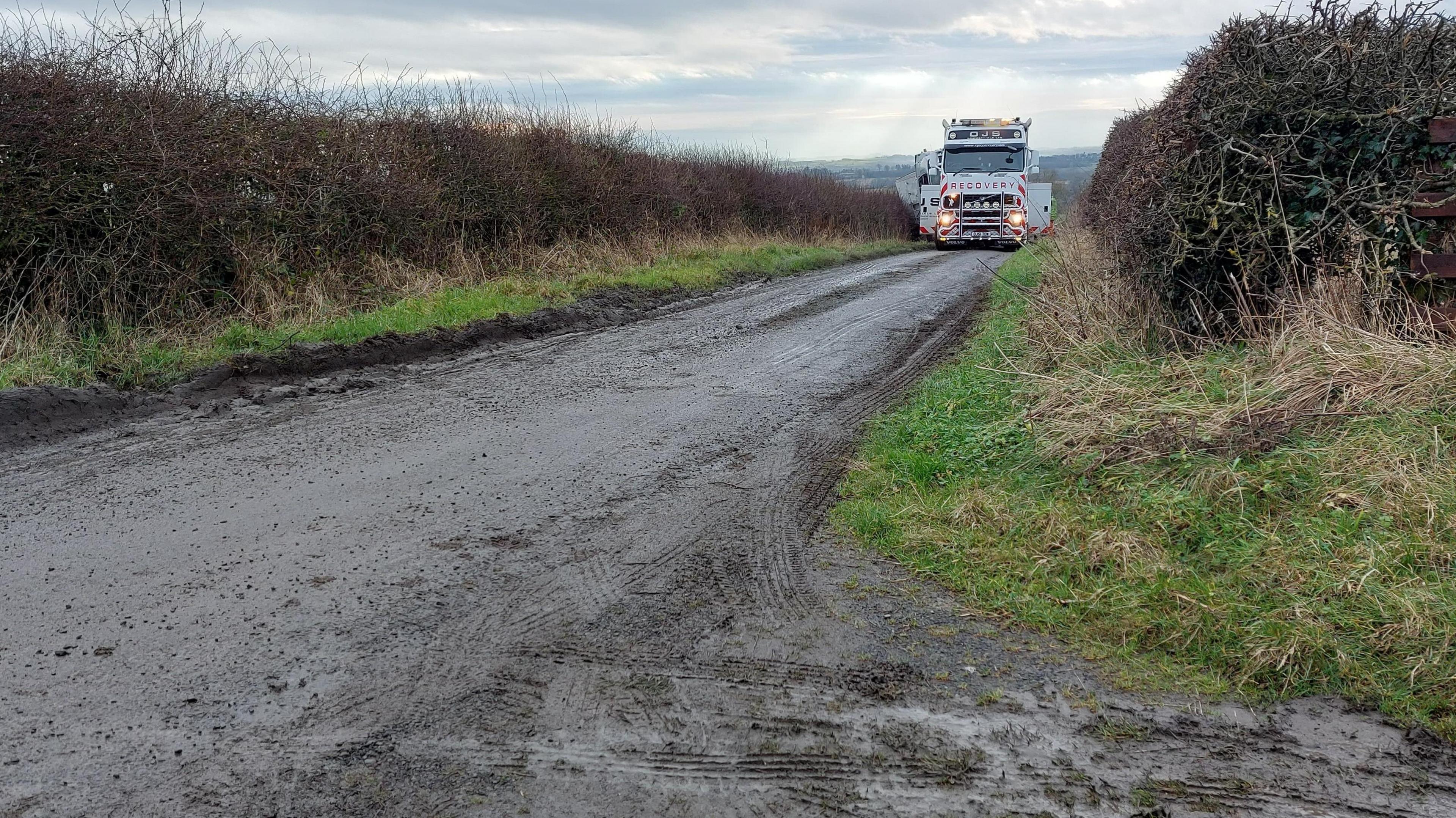 A rural road with a lorry in the distance which appears to be blocking the whole road 