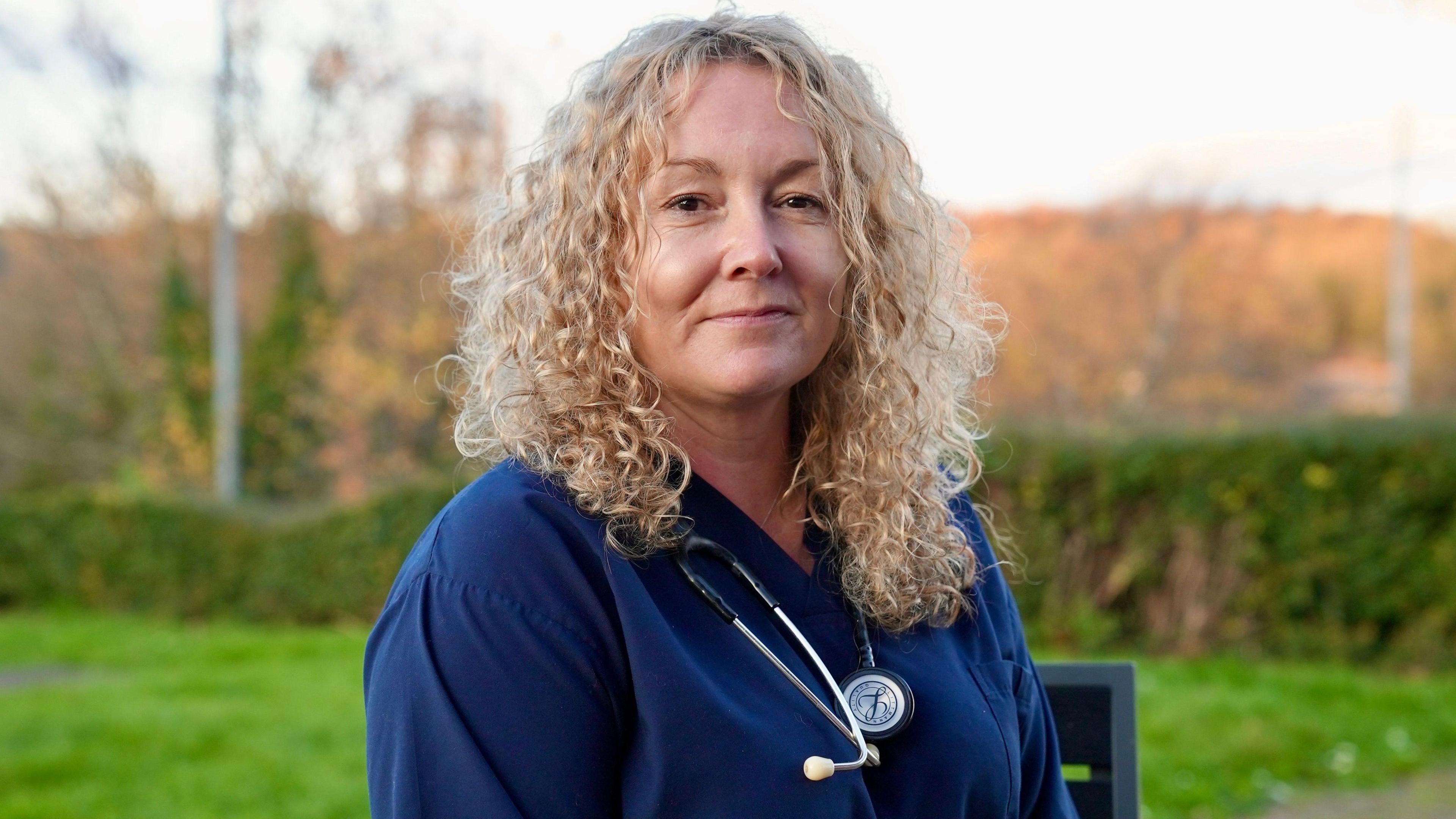 Dr Samantha Jenkins is wearing her medical scrubs and stethoscope and is posing for a picture with the countryside behind her.