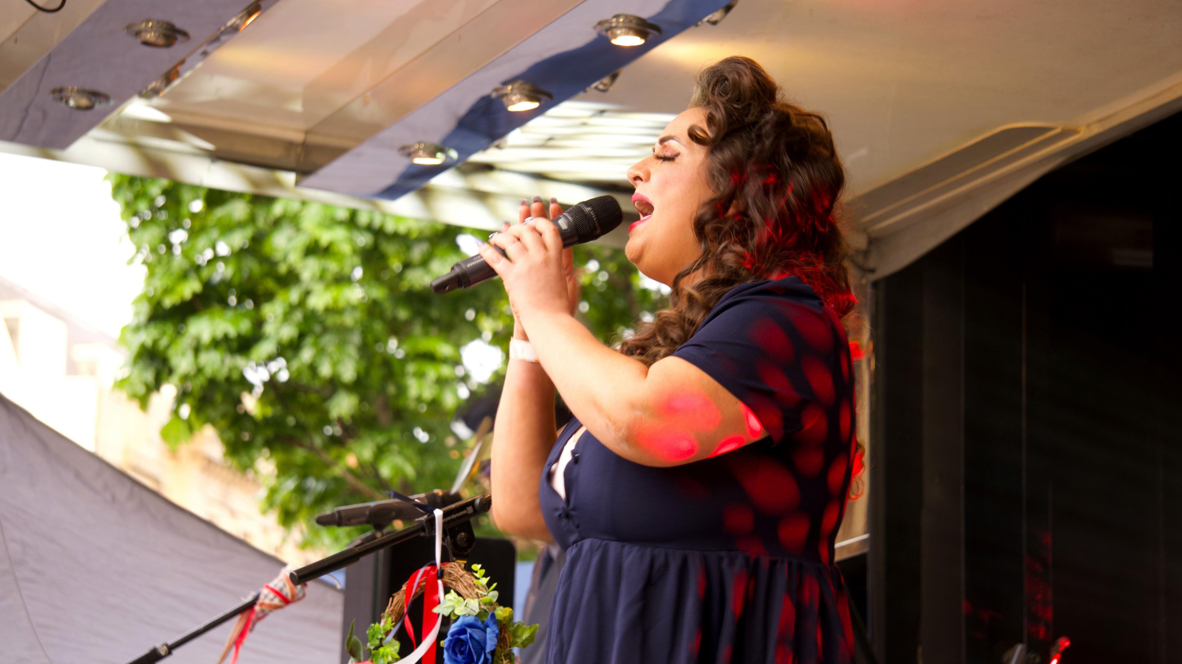 A singer in a blue dress with long brown hair holding a microphone on stage