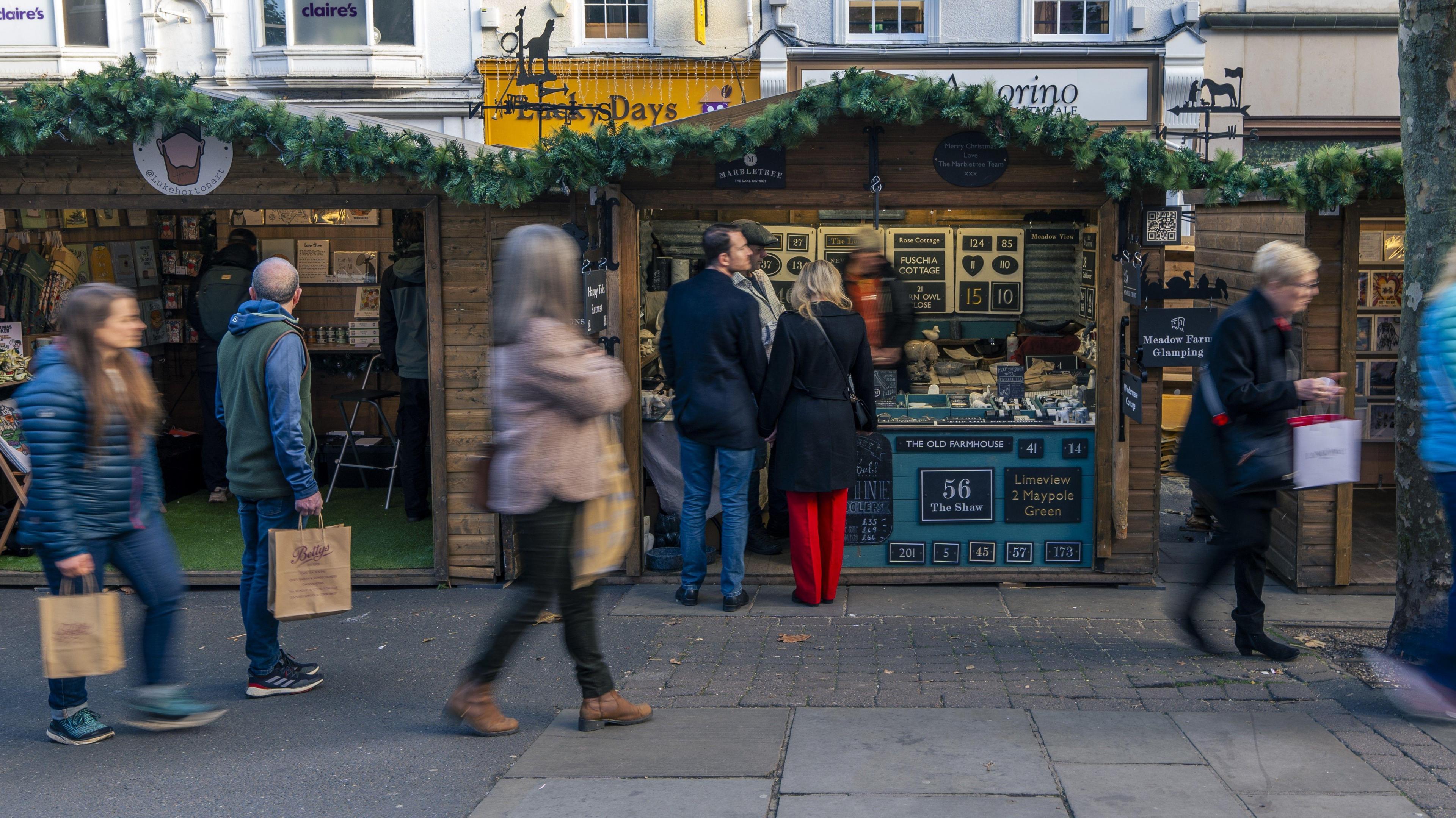 People walk past wooden chalet-style buildings selling a range of Christmas gifts, at York Christmas Market.