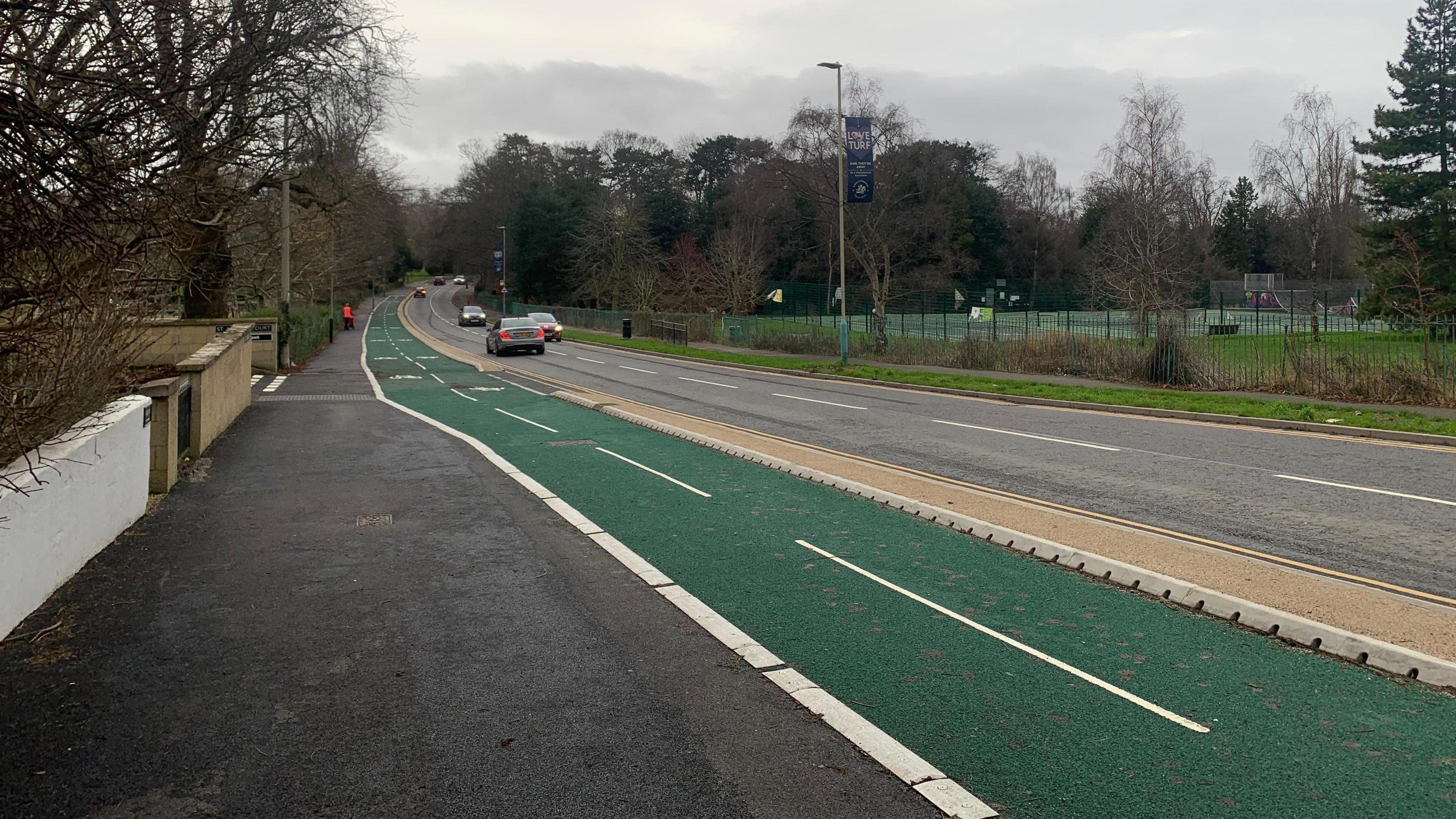 A black tarmac pavement, next to a green cycle lane, beside a road.