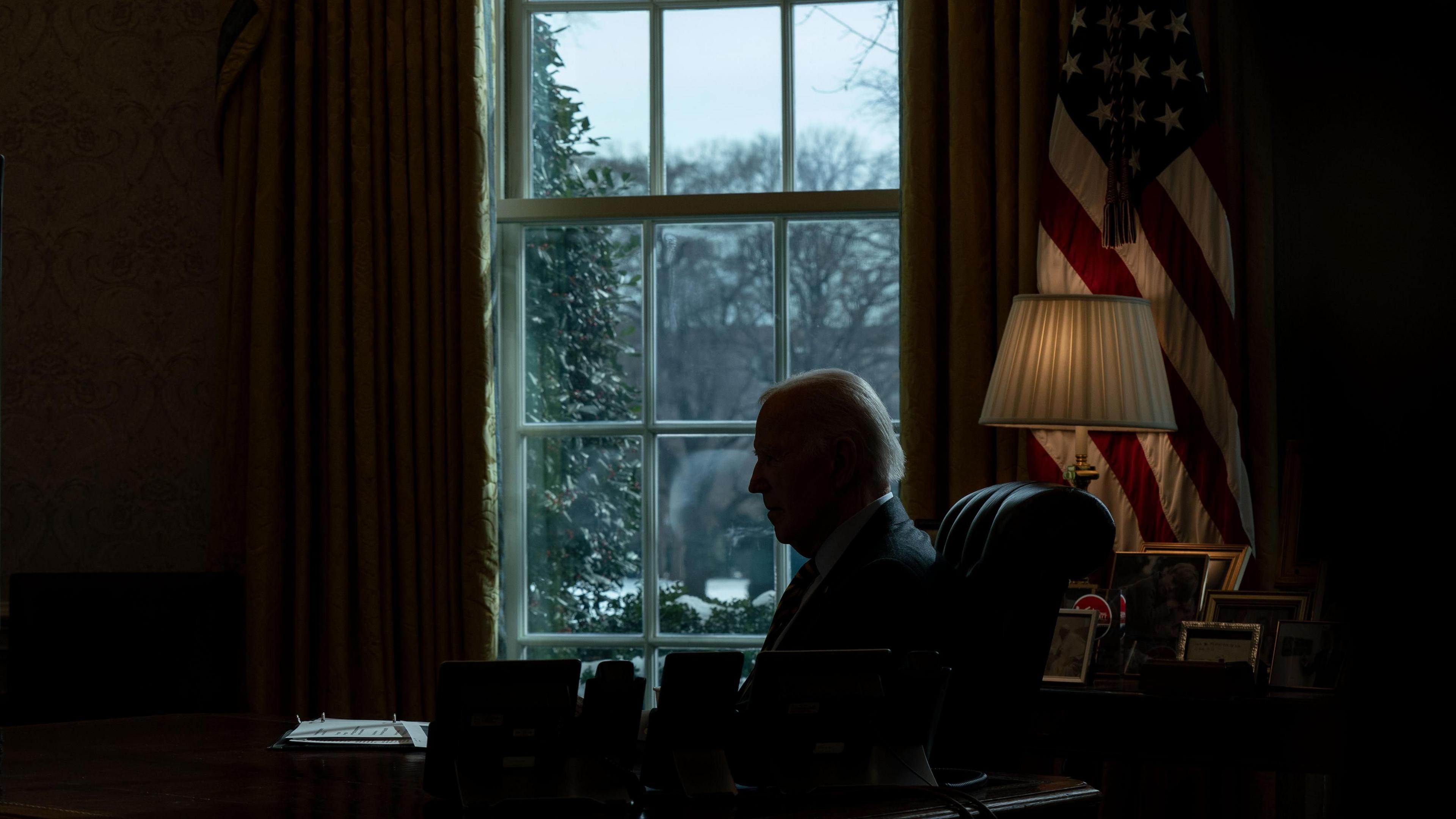 President Joe Biden receives a briefing at his desk in shadows