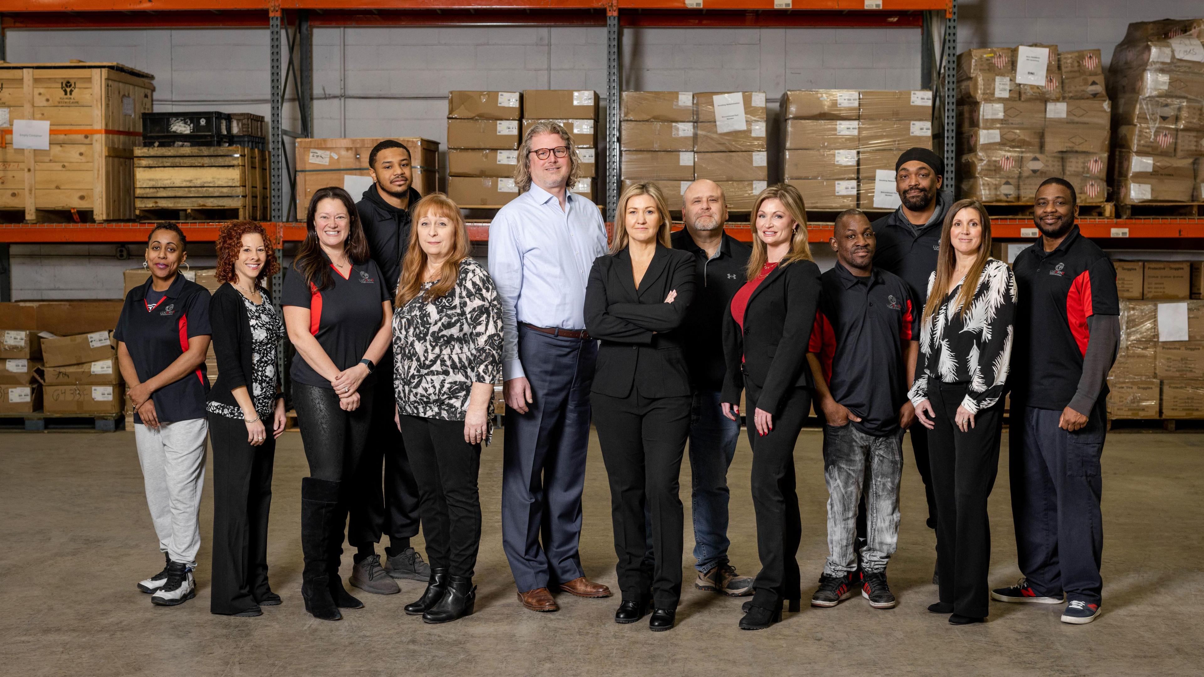 Mary Buchzeiger (centre) stands in a row with her team at a Lucerne International warehouse. The team look at the camera, with carboard boxes piled up on shelves behind them.