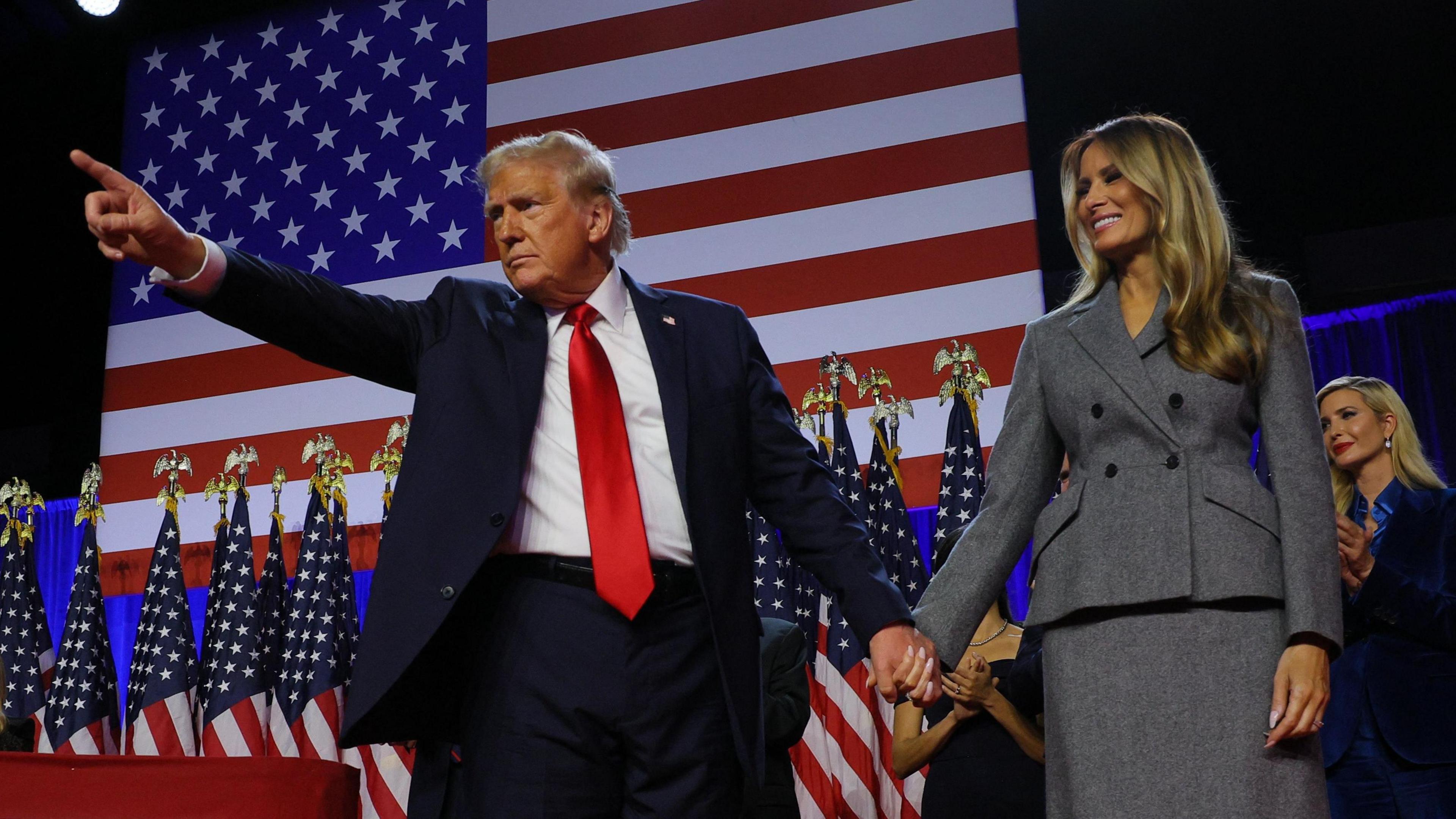 President Donald Trump points while on stage, in front of an American flag, as he holds hands with his wife Melania during his rally at the Palm Beach County Convention Center in West Palm Beach, Florida, U.S