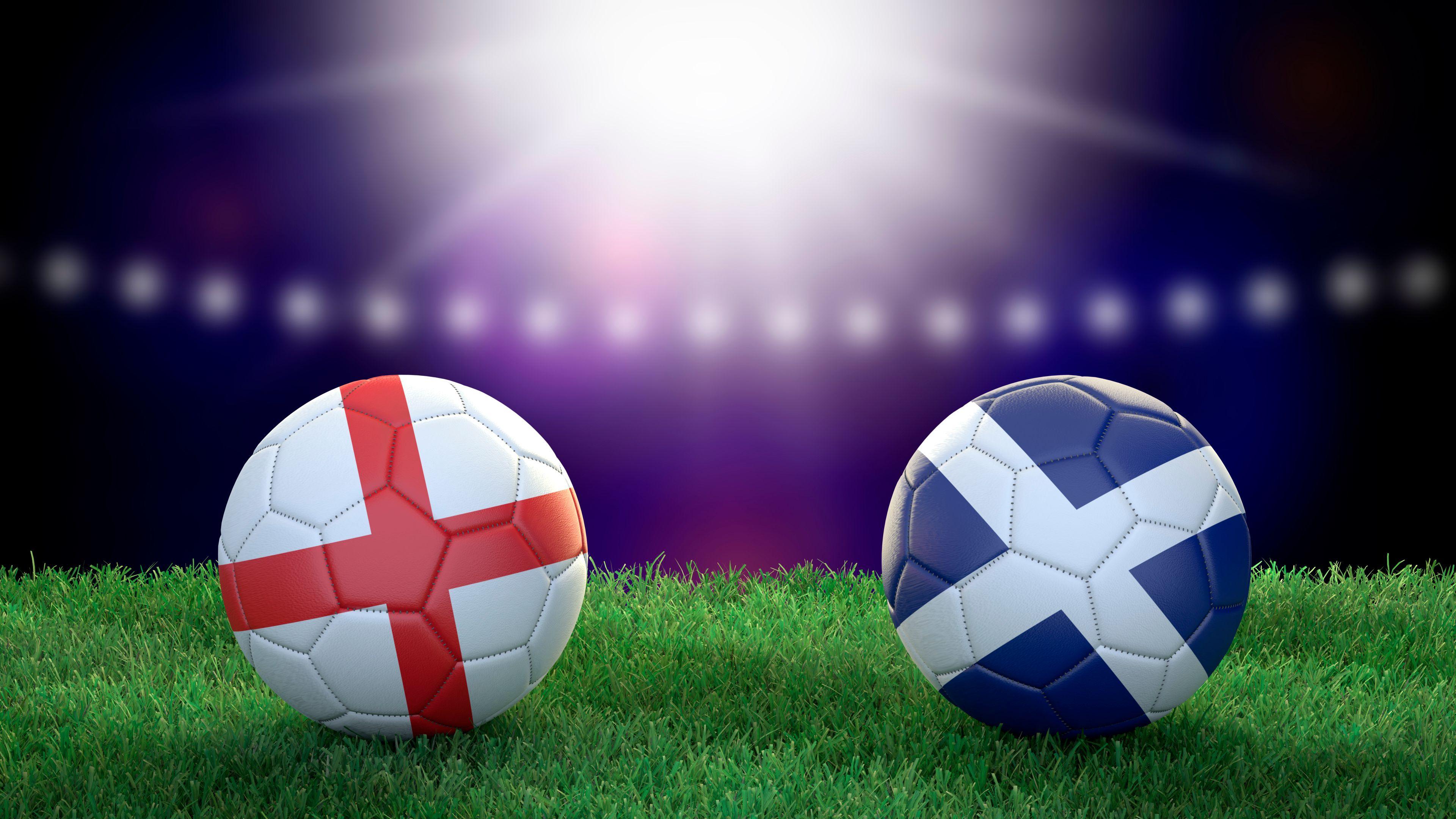 Scotland and England flags on footballs on a grass pitch.