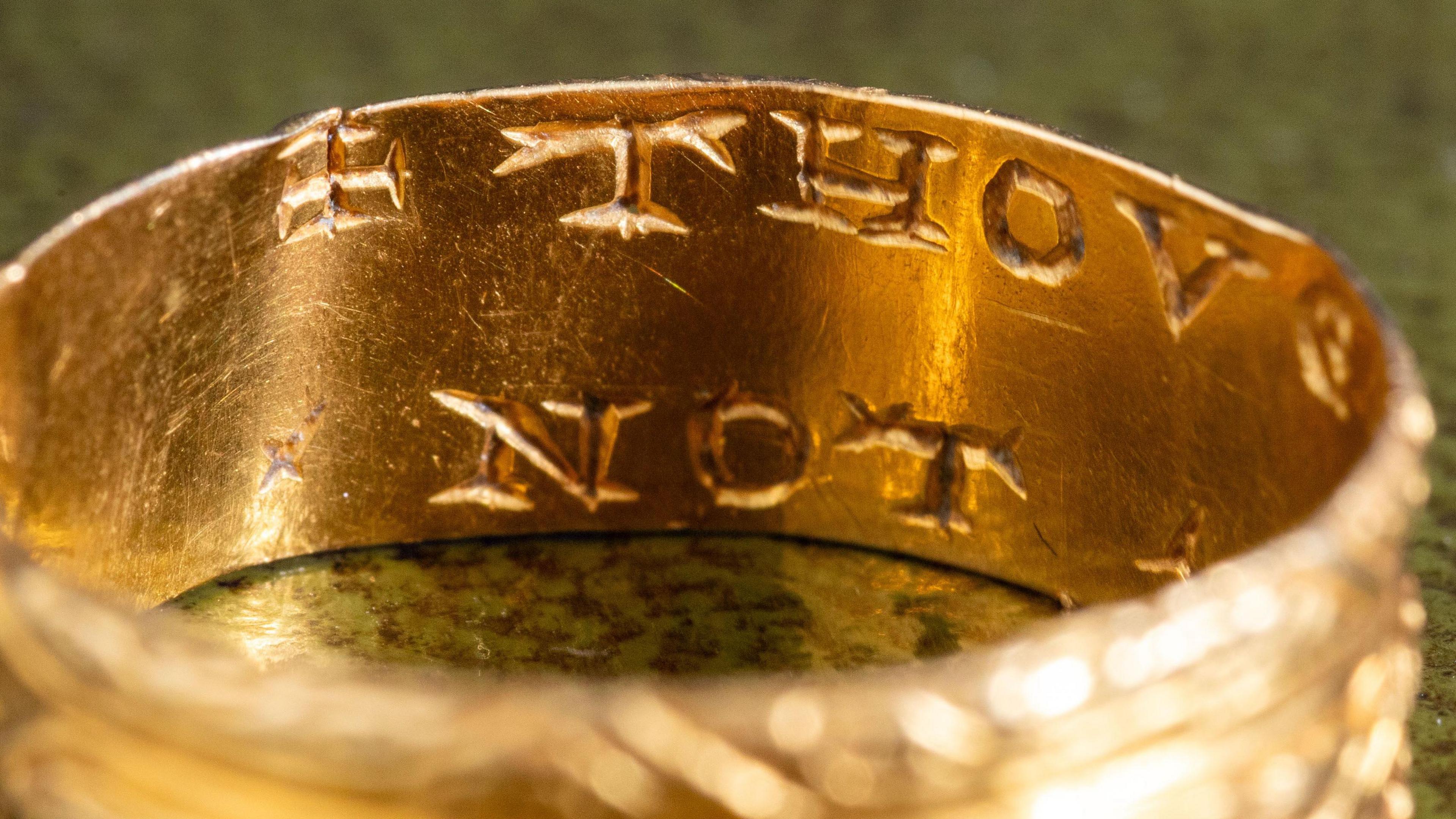 Close-up picture of the inside of the gold ring, with engraved letters of the words "THOU" and "NOT". Some decoration is visible on the outside of the ring.