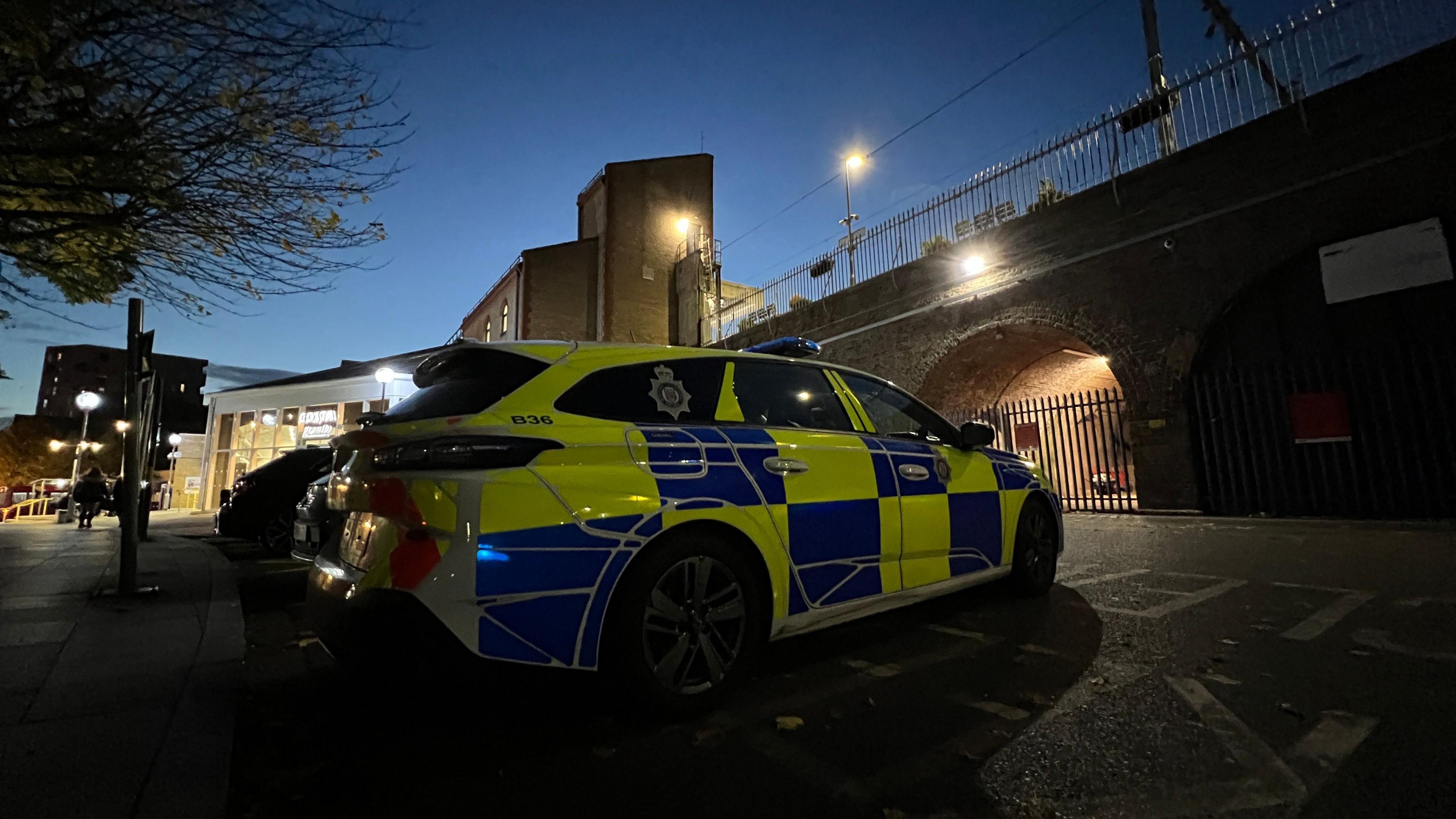 A police car parked outside Chelmsford Railway Station. The sun is setting into the photo.