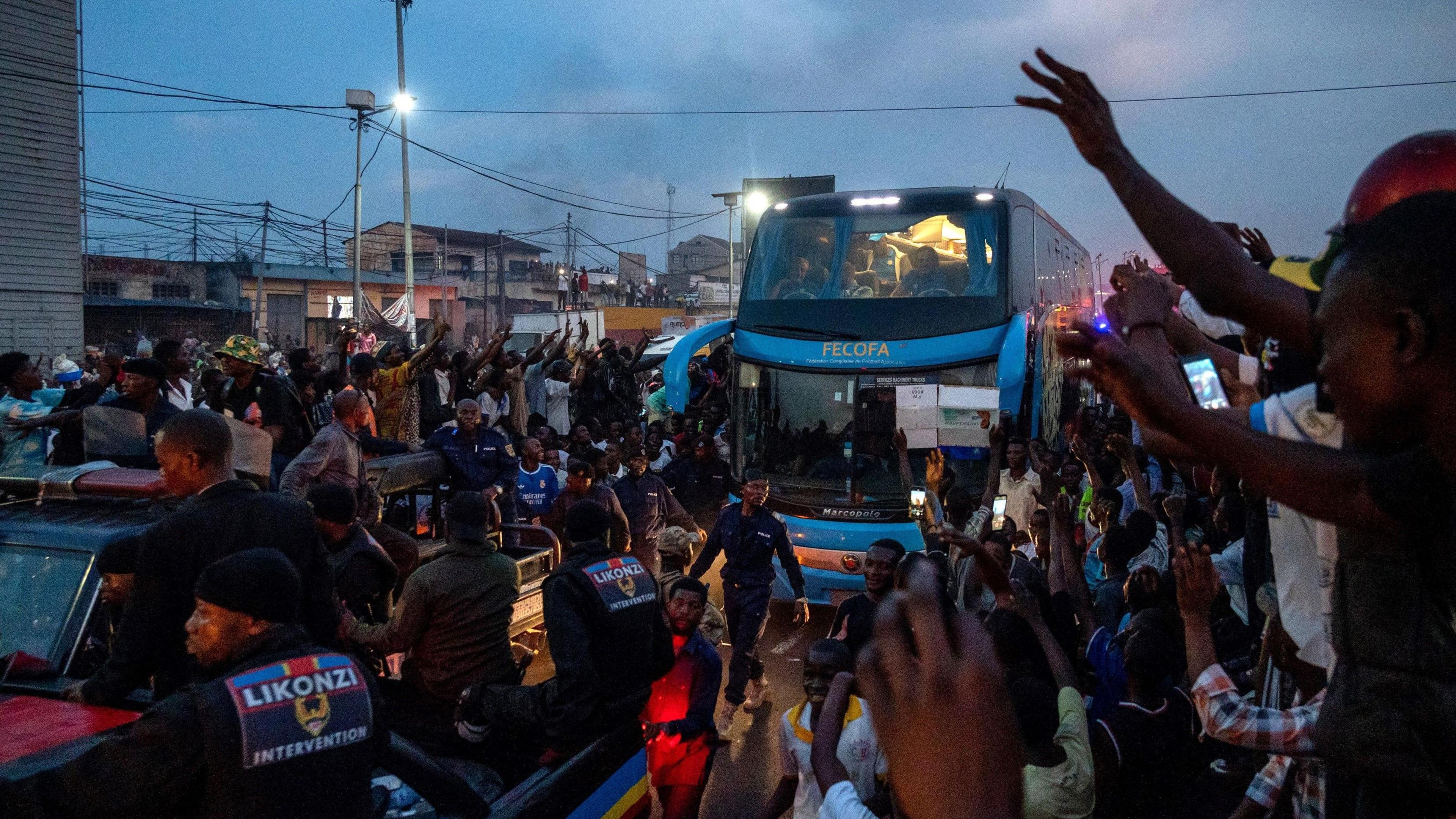 Fans of DR Congo line a street as a coach carrying the team drives down a road
