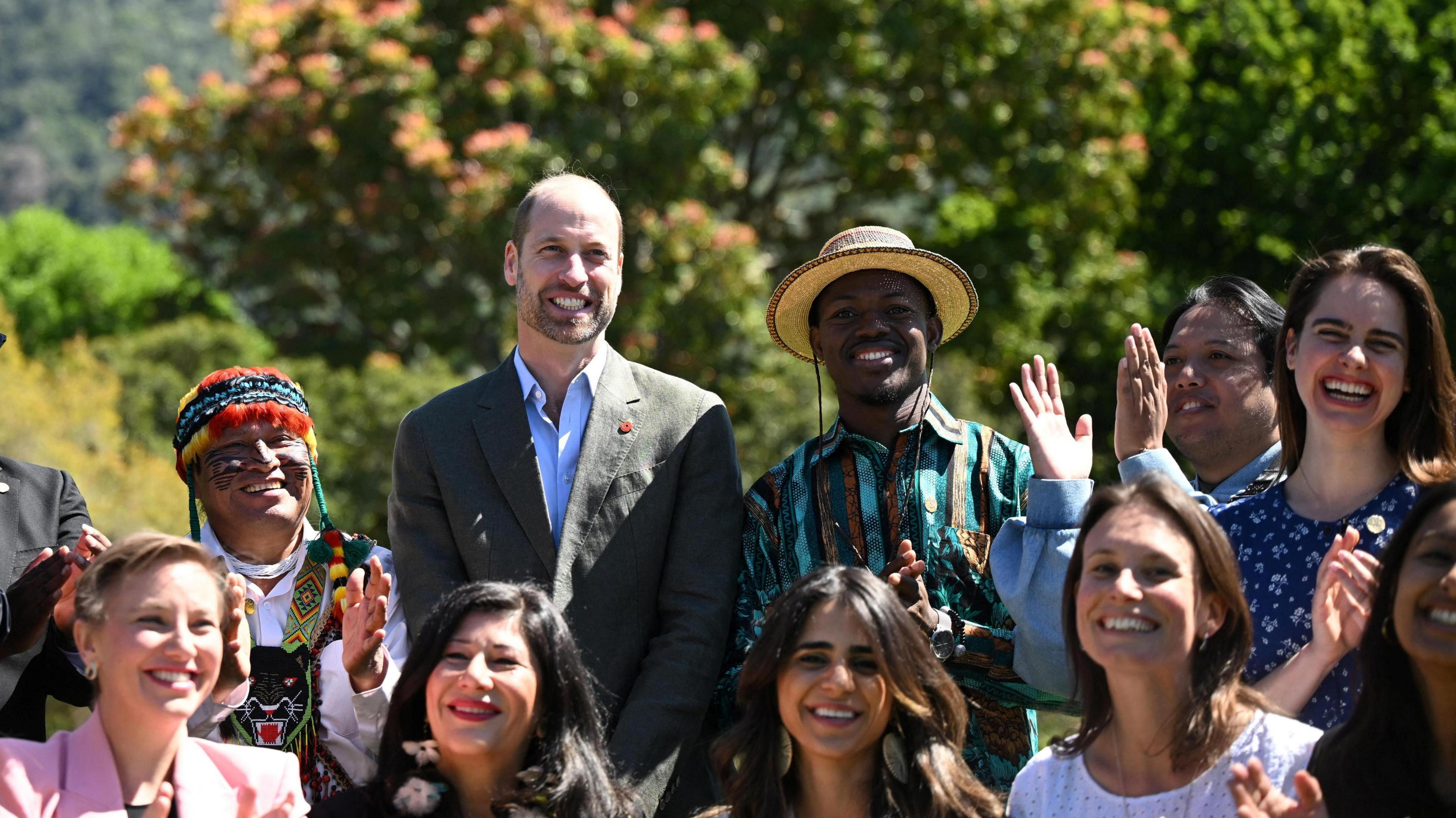 Prince William smiles in a group photo with the finalists of the 2024 Earthshot Award. Seven women and three men surround him, they are all smiling and applauding.