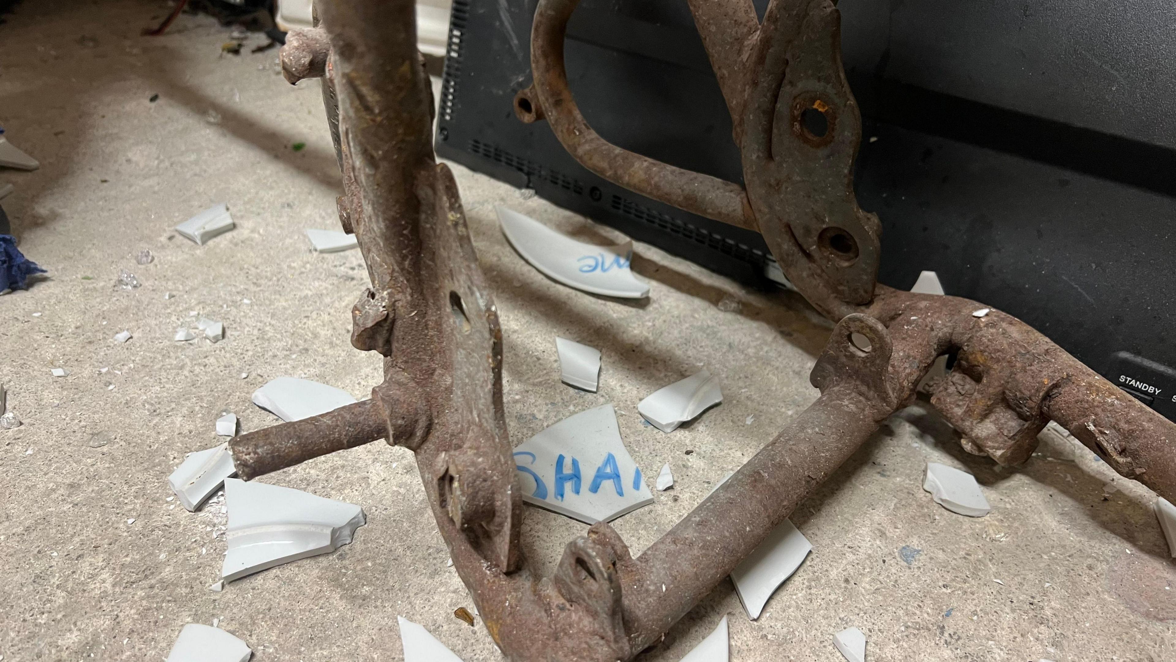 A smashed plate on the floor. One of the broken pieces has the words 'SHA' which did say 'shame'. 