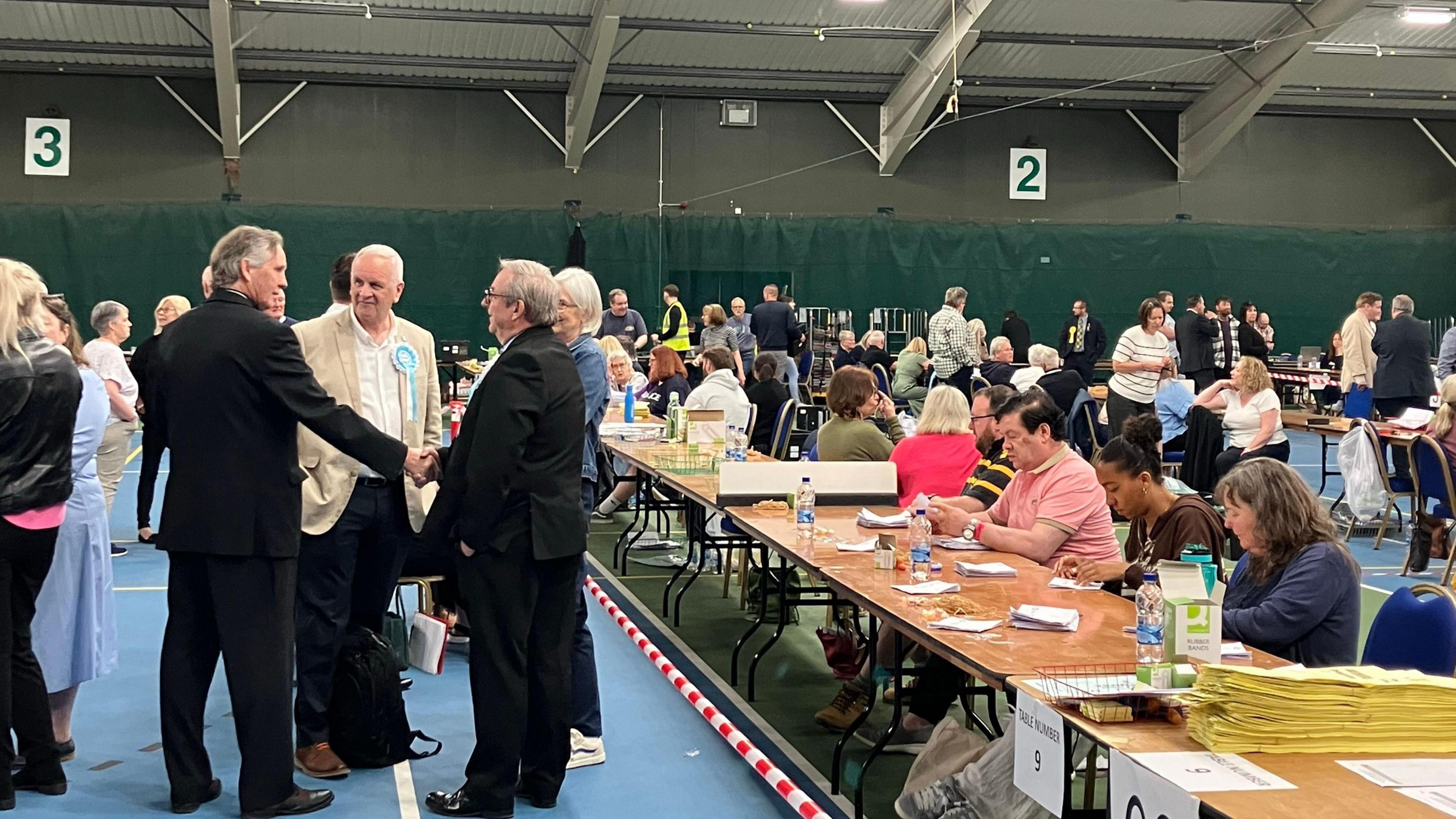 Inside a hall during the election count. People are sitting at tables for the count.