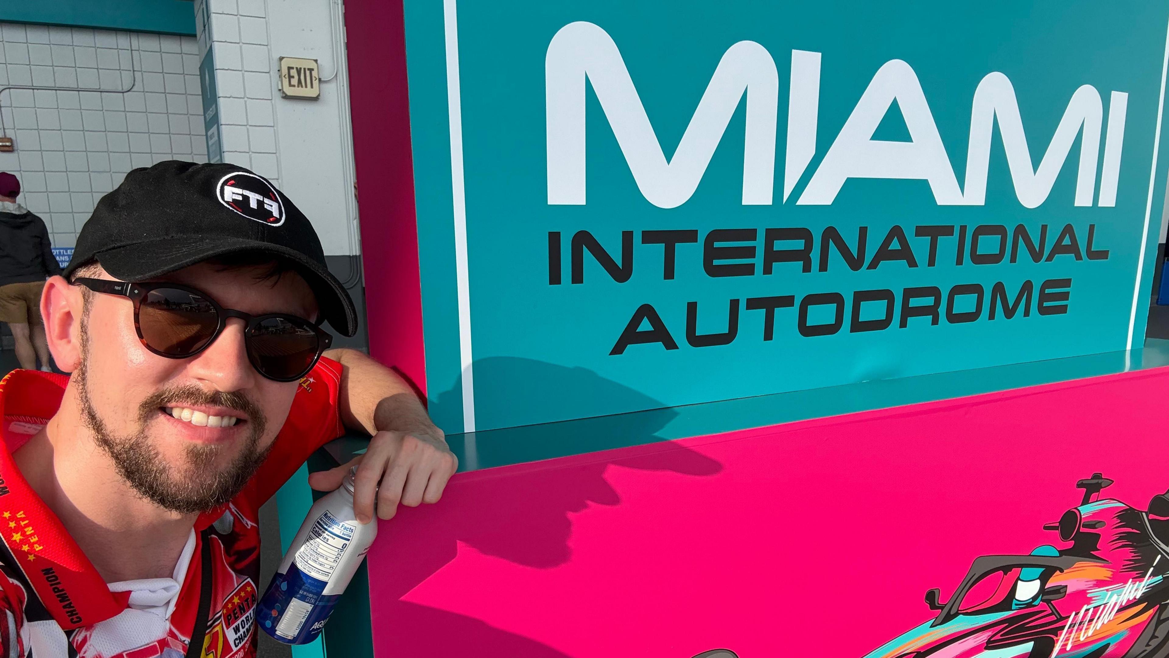 Brandon Burgess poses for a selfie alongside a 'Miami International Autodrome' sign