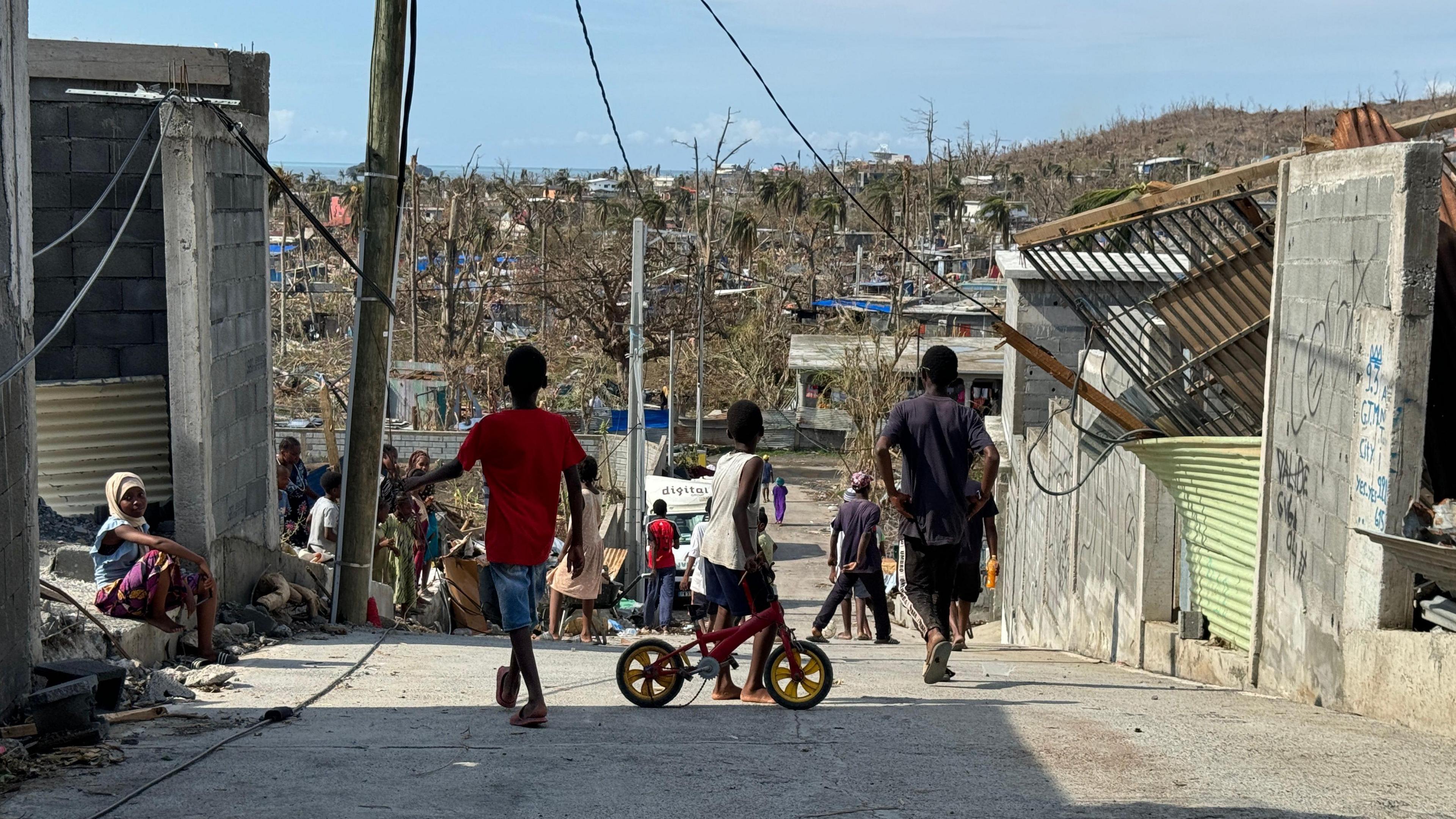 Children in the foreground on a road with damaged buildings behind