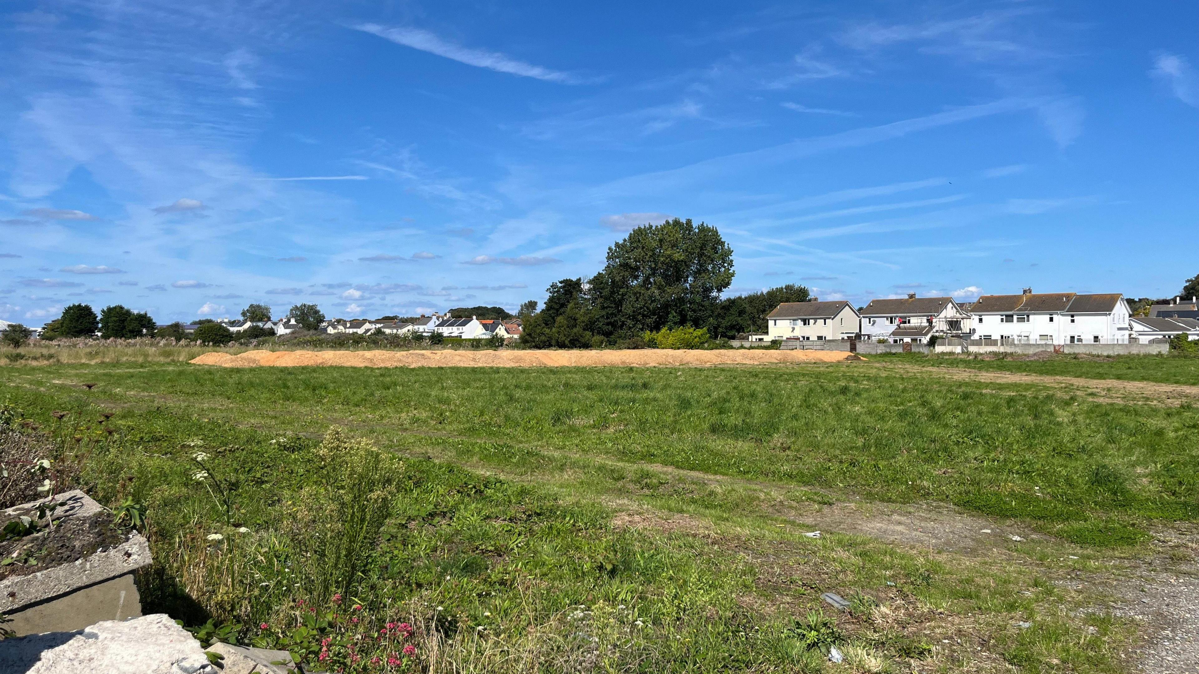 A green field with a long mound of dirt in the distance. 