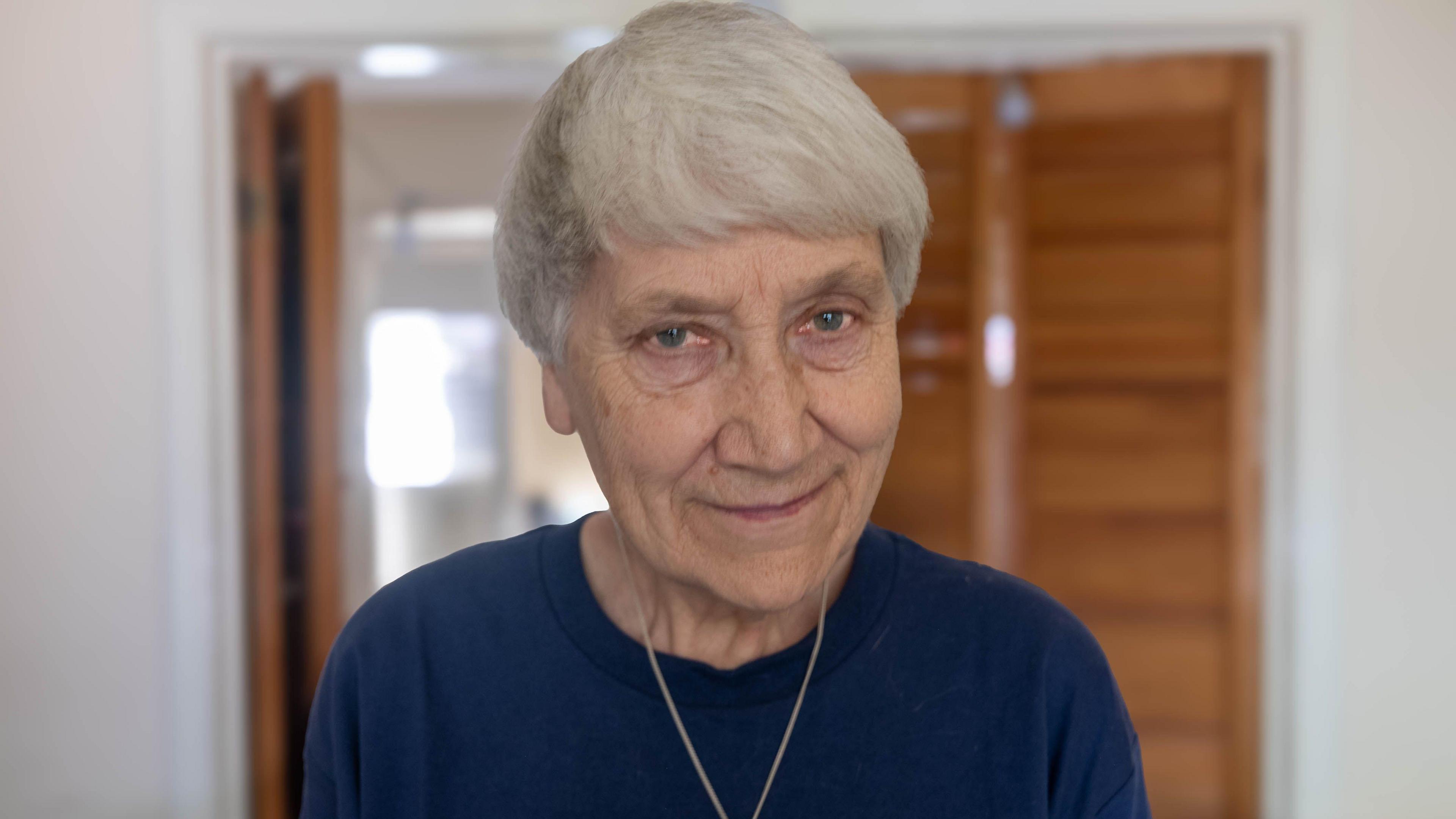 Mary Joy Langdon, 76, smiling for the camera in an interior room. She is wearing a dark-coloured jumper.
