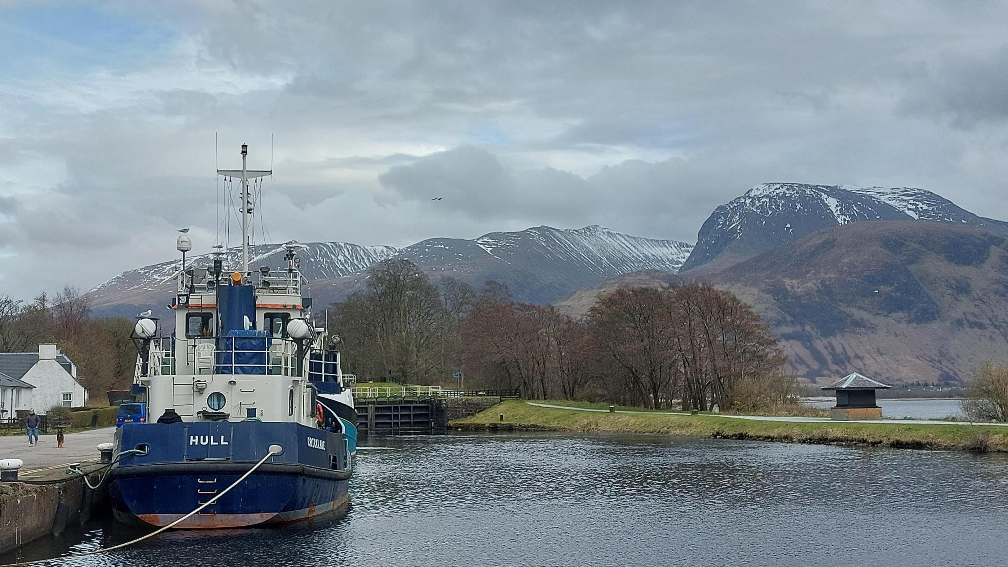 View looking across a loch in Highland Scotland with a fishing vessel. In the background are mountains with a small covering of snow