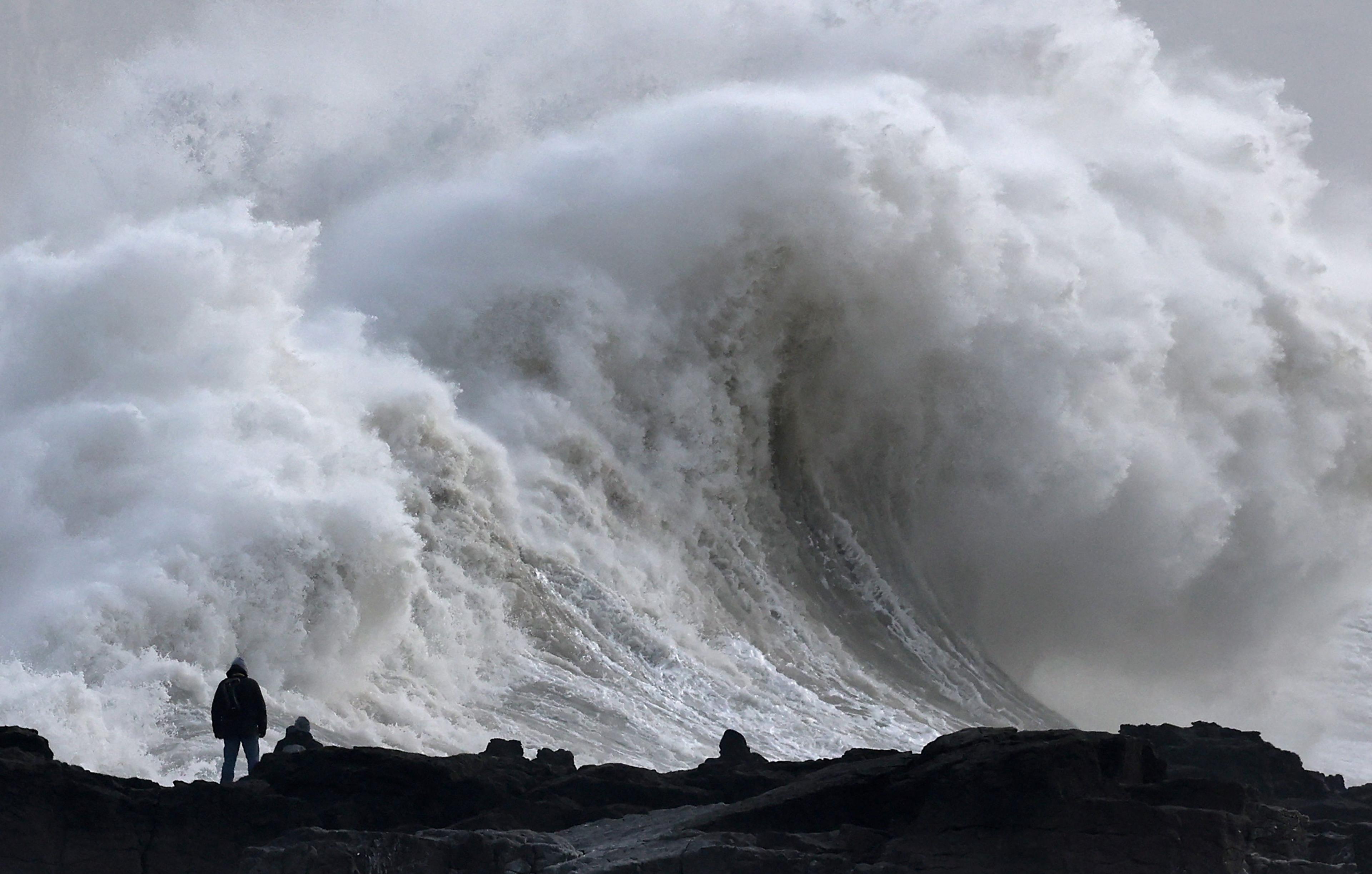 A person stands in front of huge waves in Porthcawl, South Wales. 