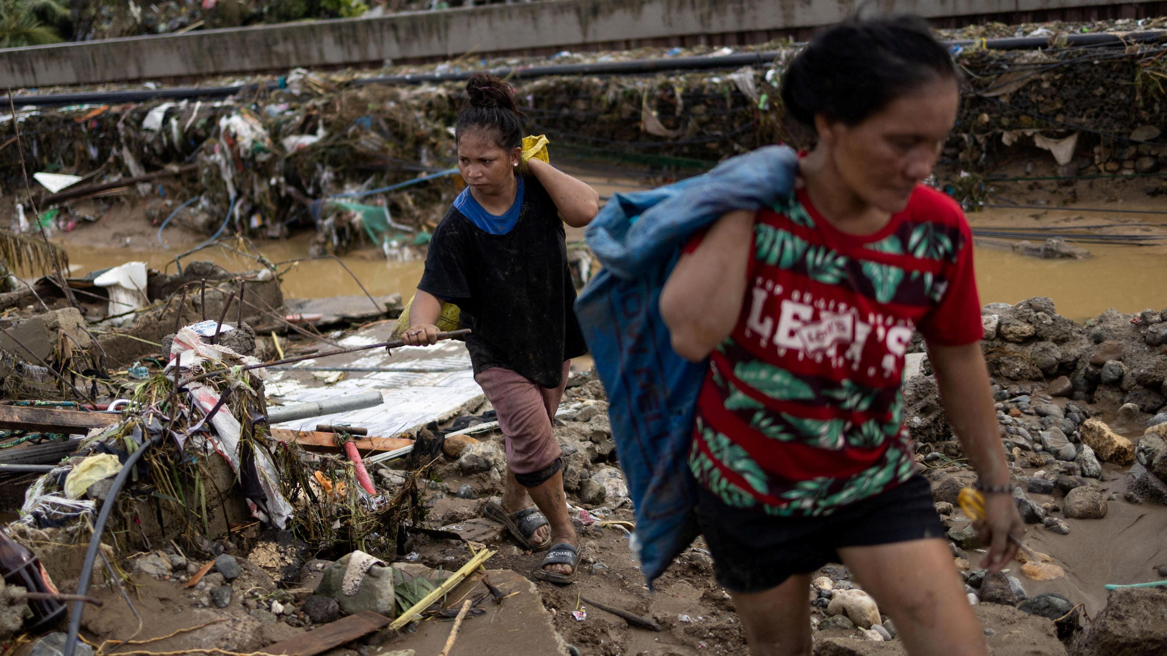 Two women return to the remains of their homes that were swept away in the floods caused by Typhoon Kalmaegi in Talisay, Cebu. Around them there is brown water and lots of mud as well as debris.