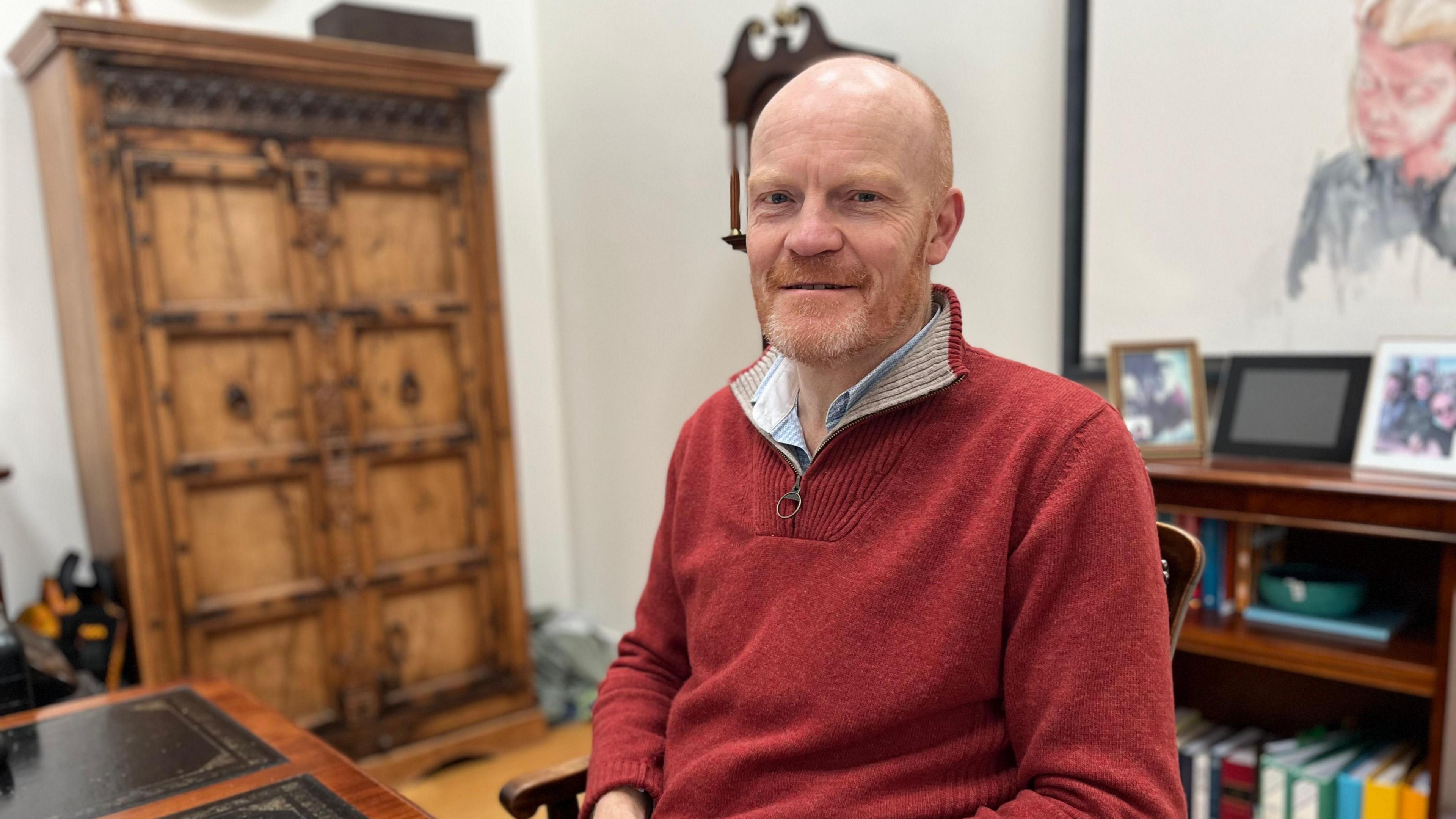 A man in a red jumper looking towards the camera. 