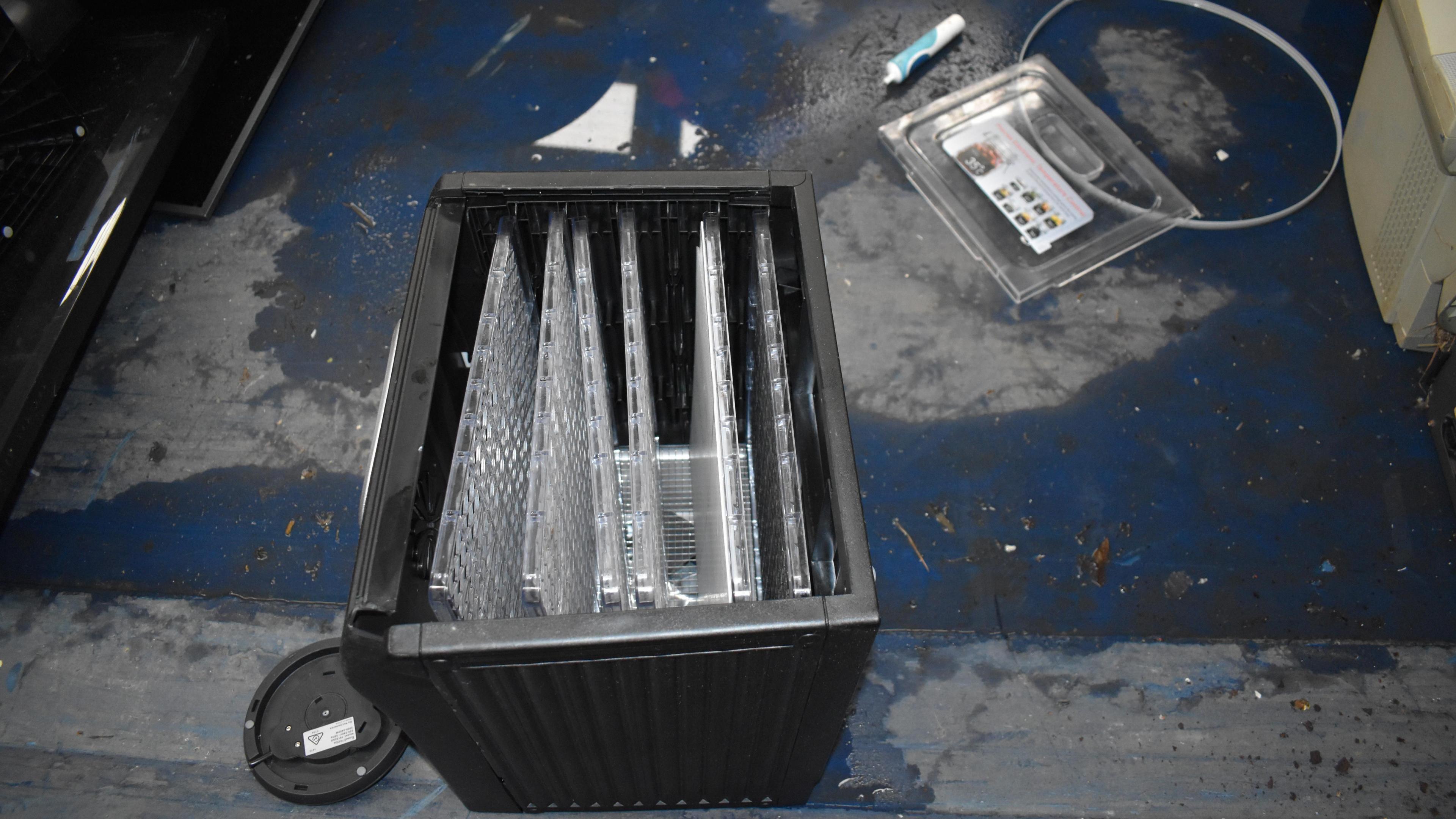 Dehydrator pictured at the tip, where it was recovered from. It is standing on its back (the opening is facing up) and the door to it is on the floor behind. There are other unidentifiable objects near it.
