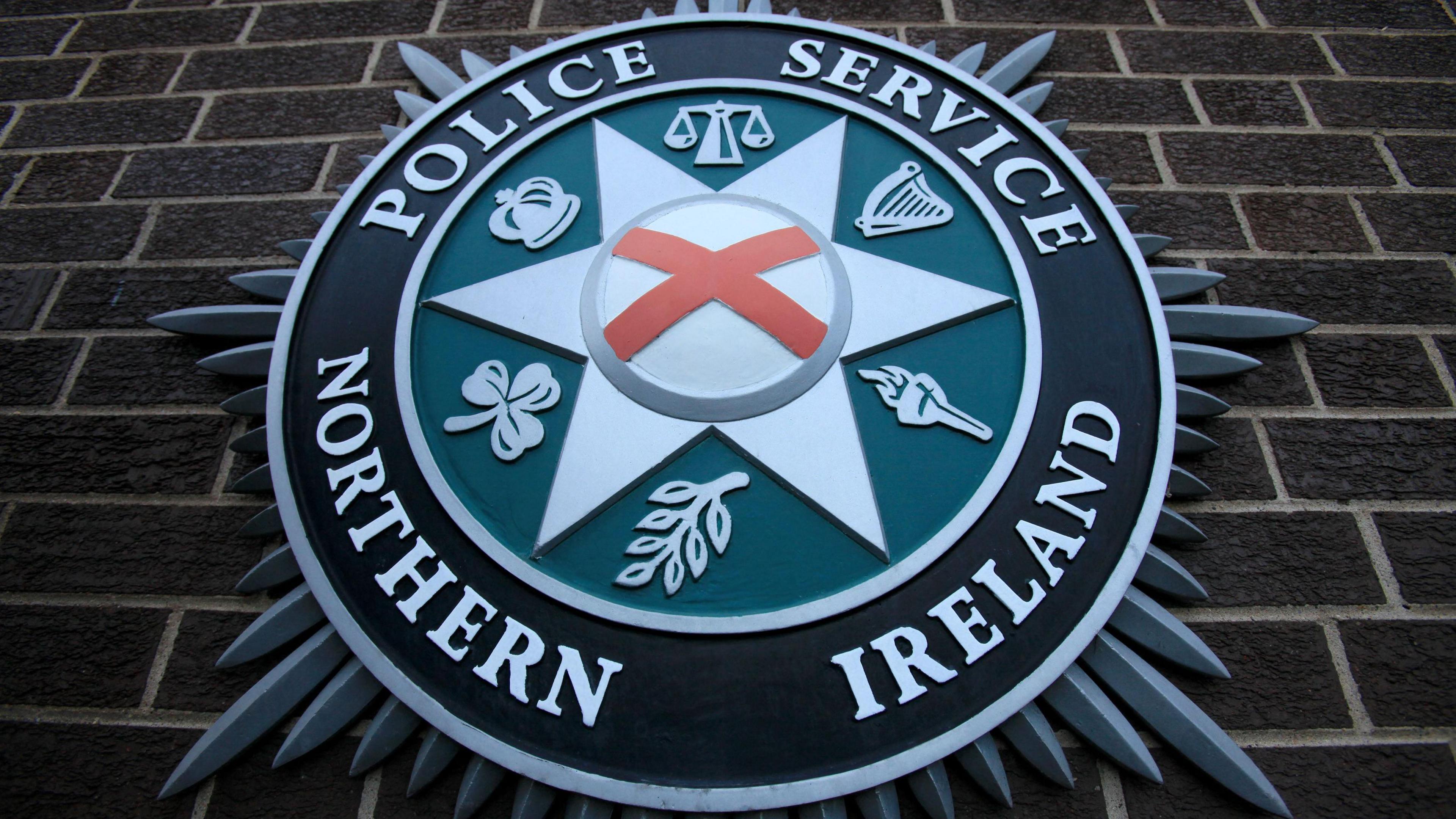 A close up of the Police Service of Northern Ireland crest against a brown brick wall