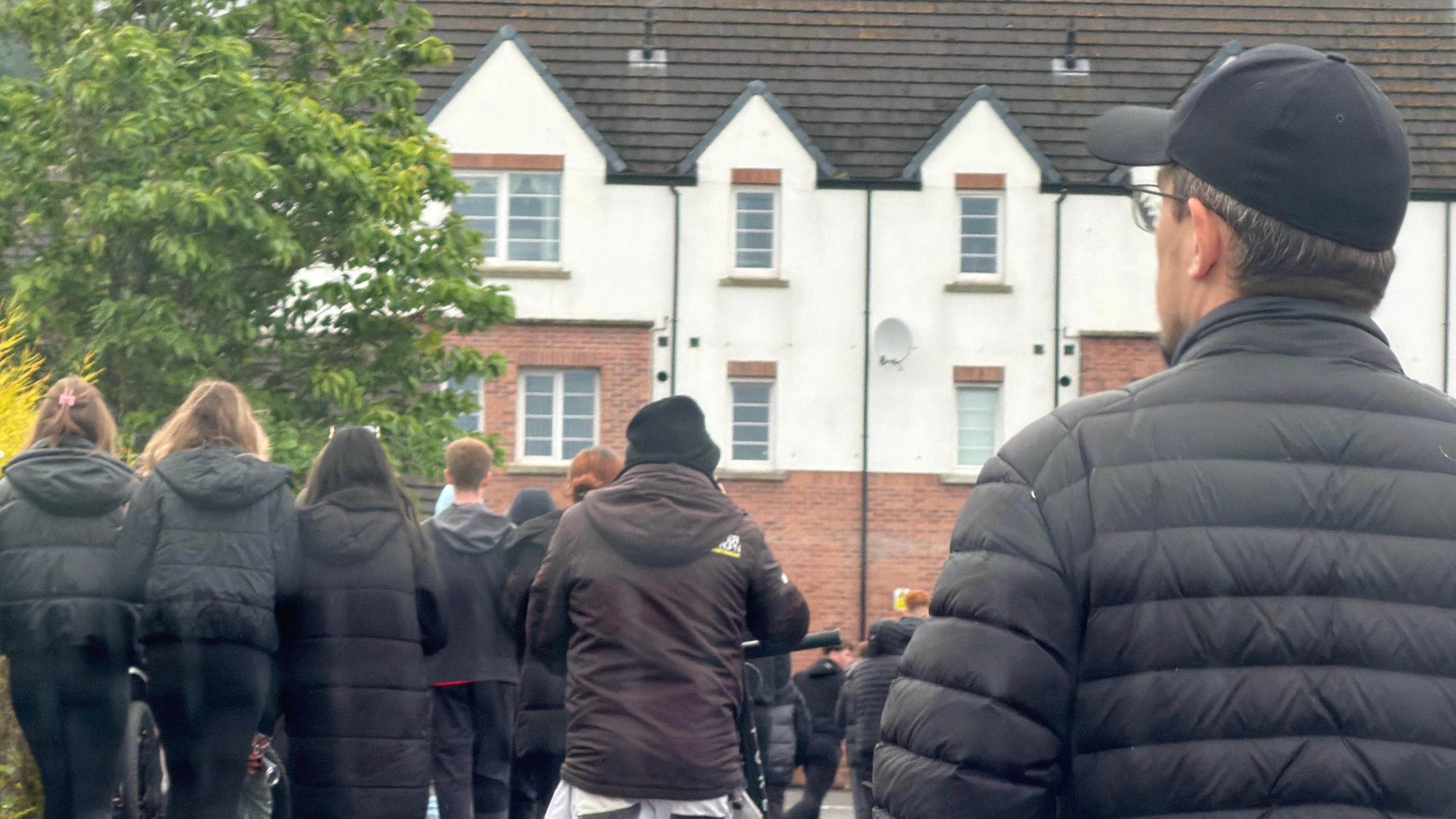 People walk through a housing estate while a man watches from the roadside.